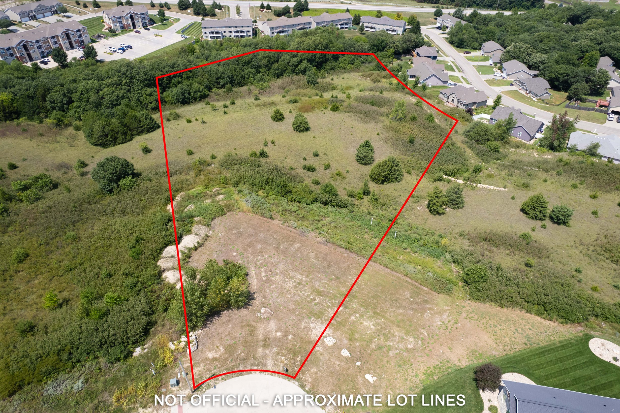 Aerial view of a vacant lot outlined in red, with neighboring residential houses and trees surrounding the area.