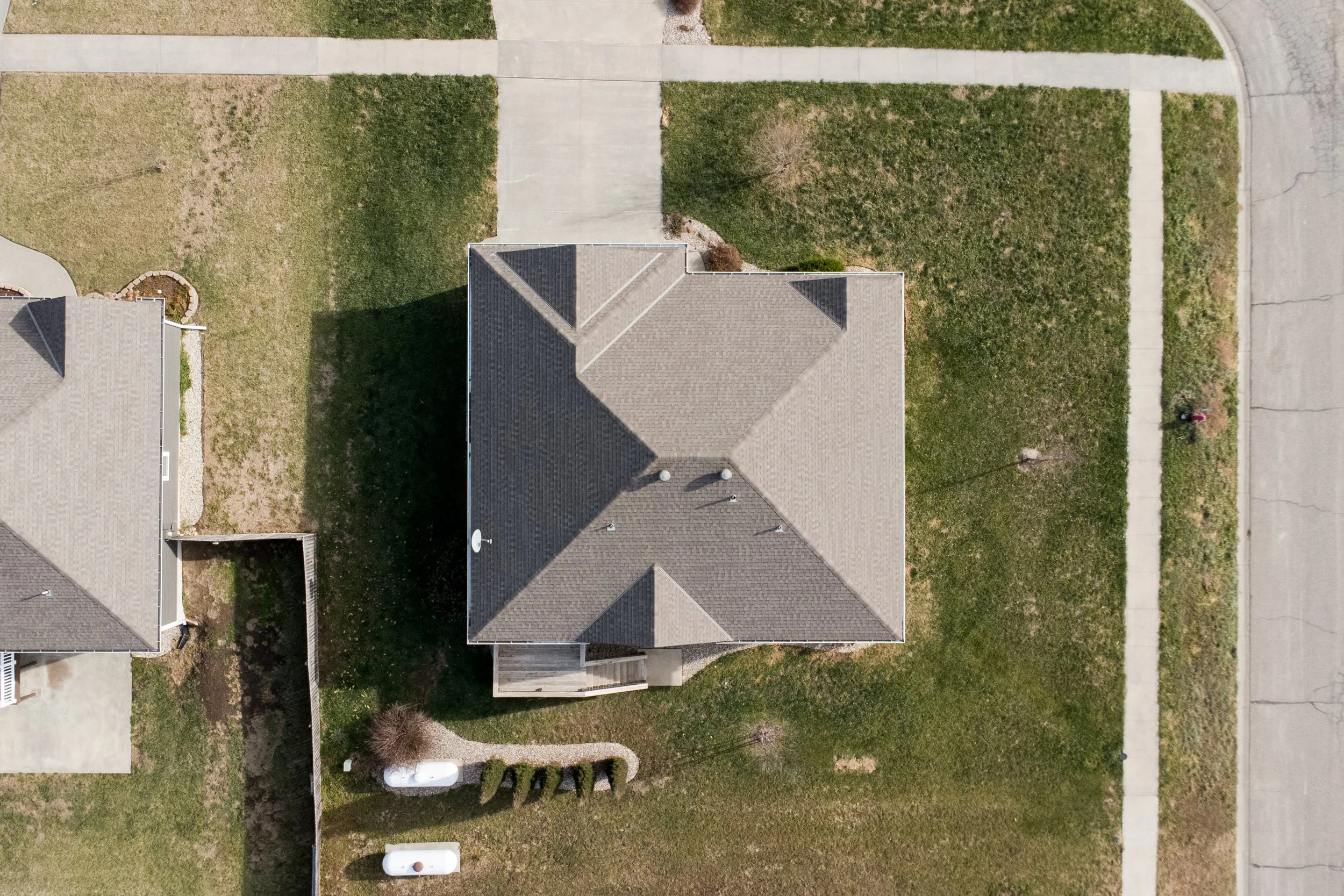 Aerial view of a house with a gray roof, surrounded by a lawn, sidewalks, and neighboring houses.