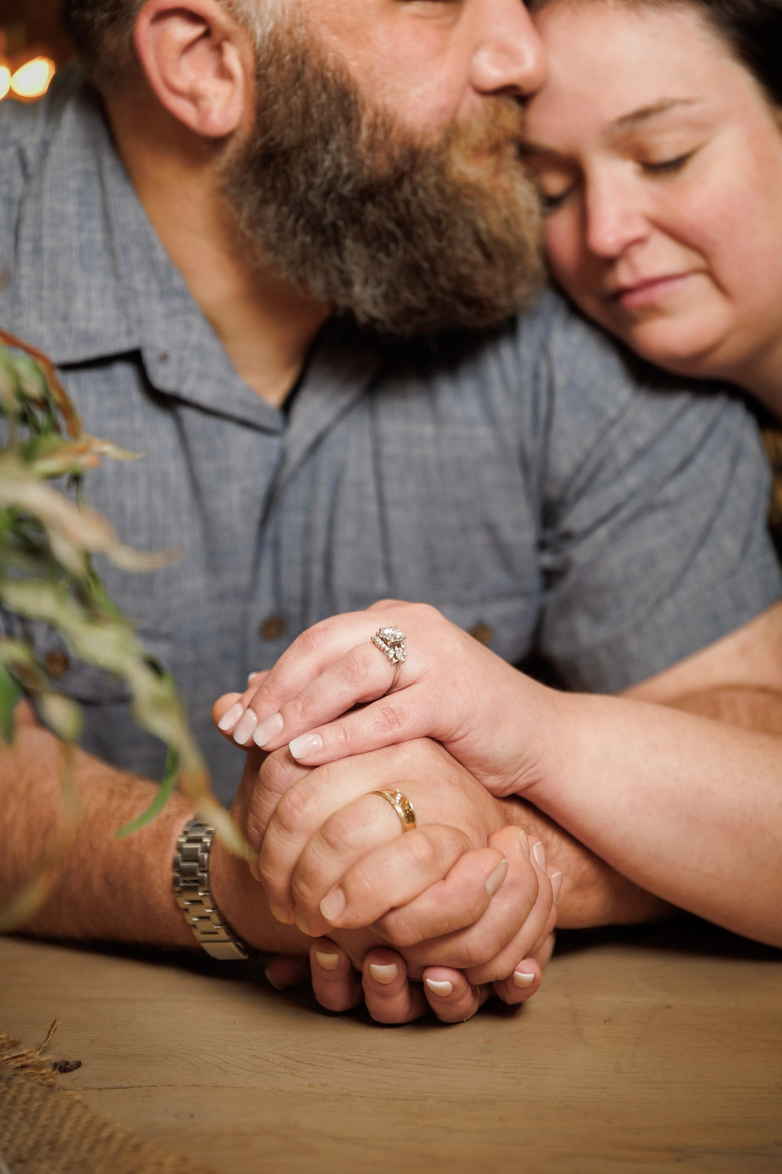 engaged couple snuggling up in an antique store with their engagement rings in focus near the camera behind a plant