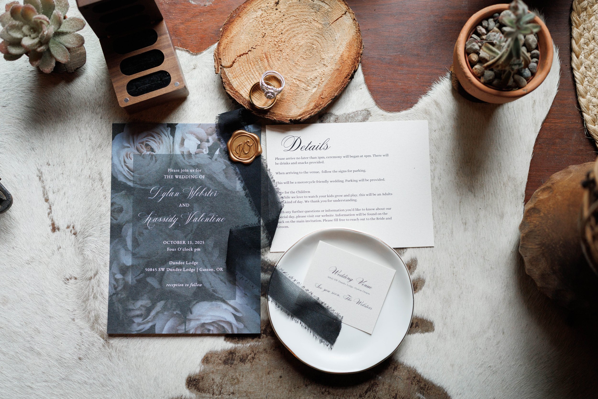 flat lay photo of wedding invitations, wedding rings, wedding box, and black ribbon, on wooden table with leather table top