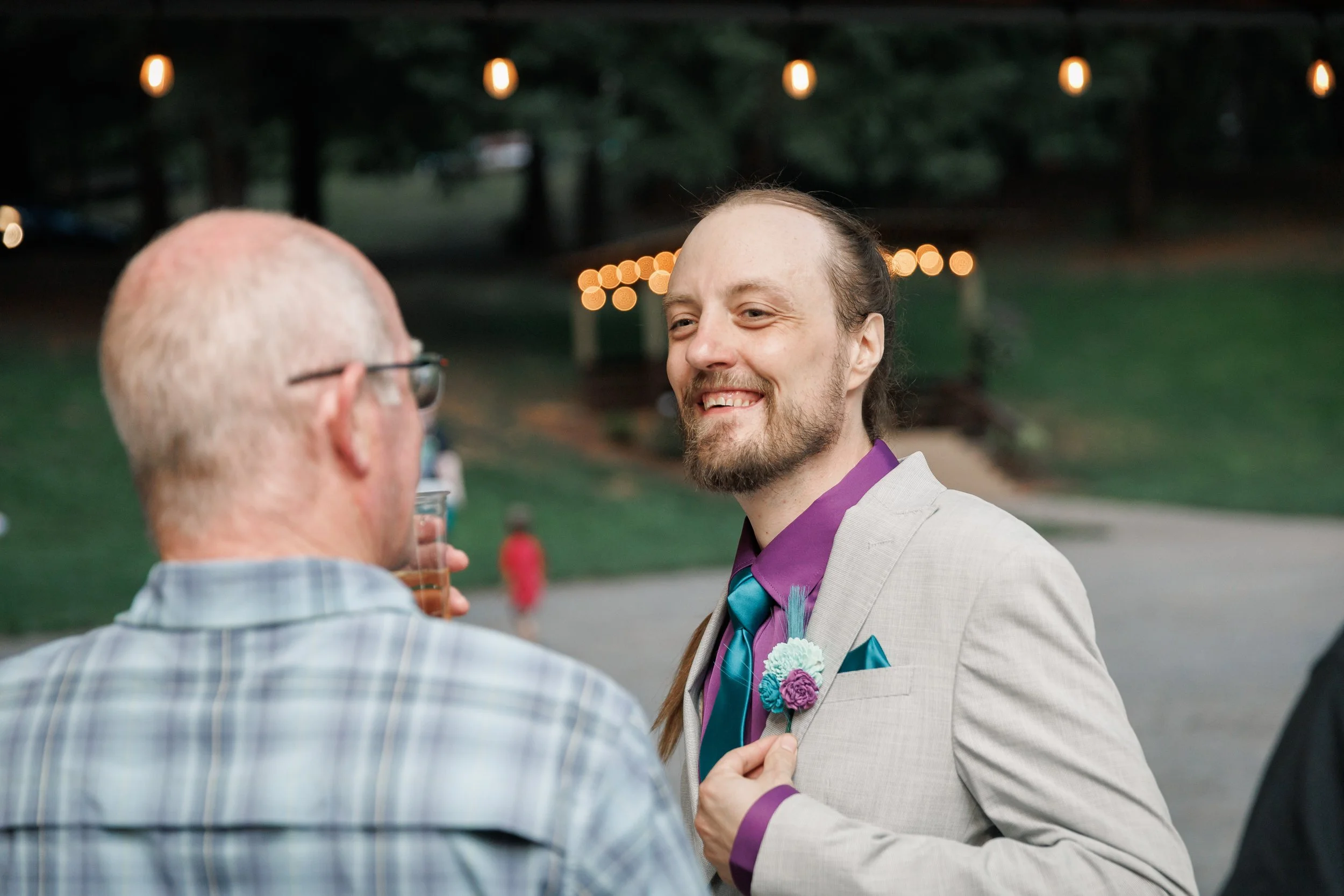 groom smiling at wedding guests in a grey and purple suit