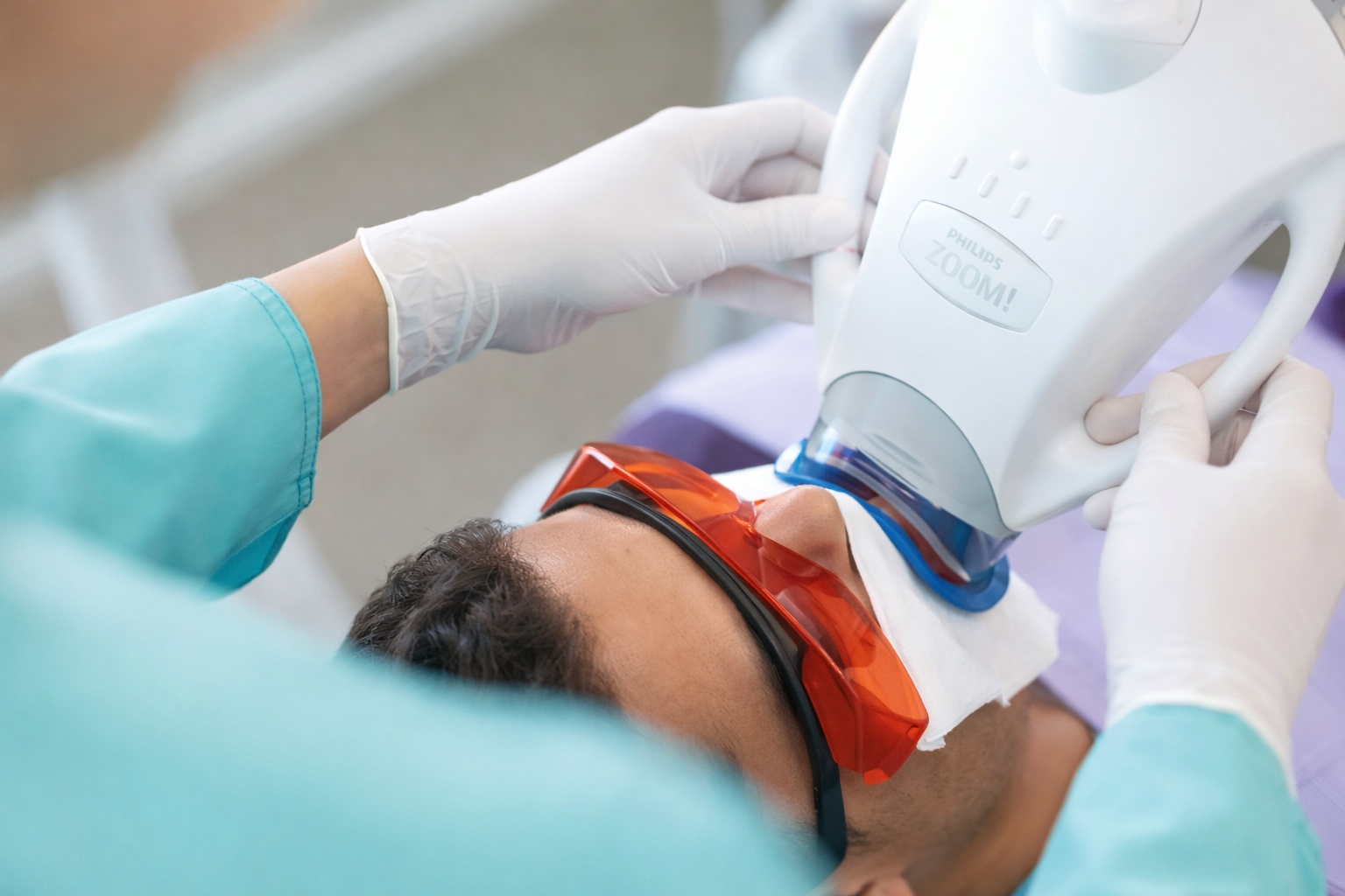 A healthcare professional using a dental X-ray machine on a patient lying down with protective eyewear.