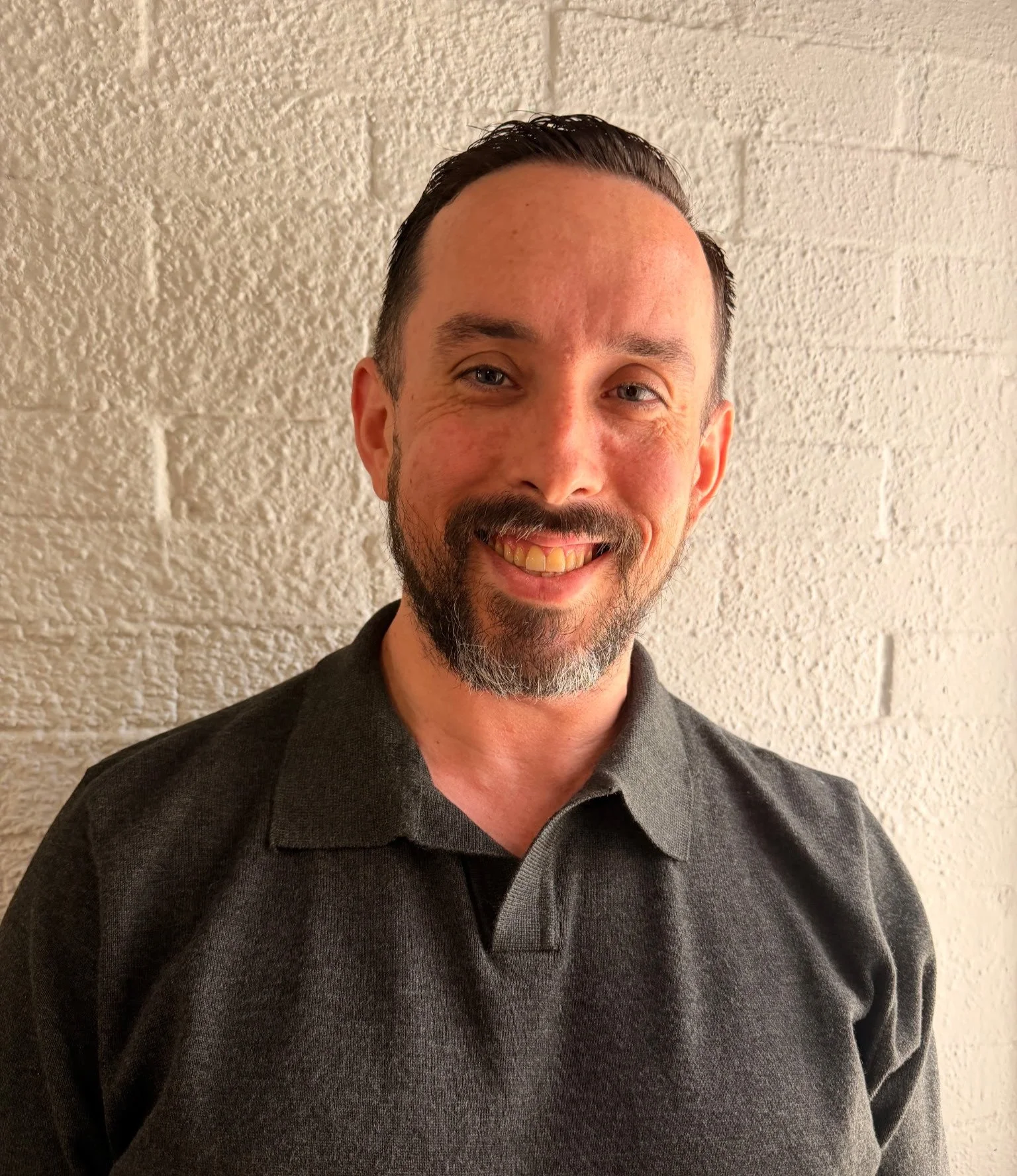 Person wearing a black V-neck shirt, smiling, against a light gray background.