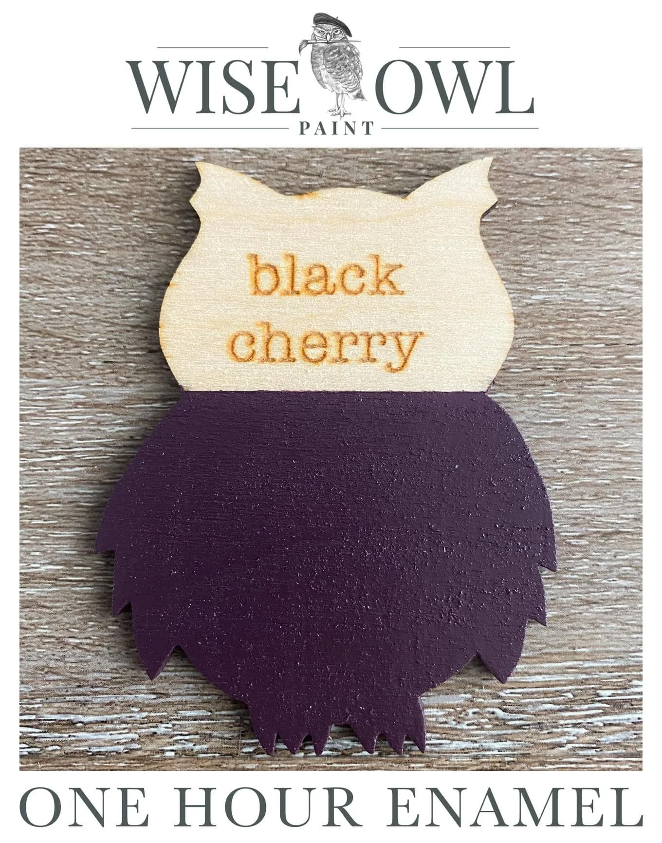 A craft art piece in the shape of a blackberry with a cream-colored top section that has orange embroidered text reading "black cherry." The bottom part is painted in dark purple to resemble the blackberry fruit. The background is a wooden surface. T