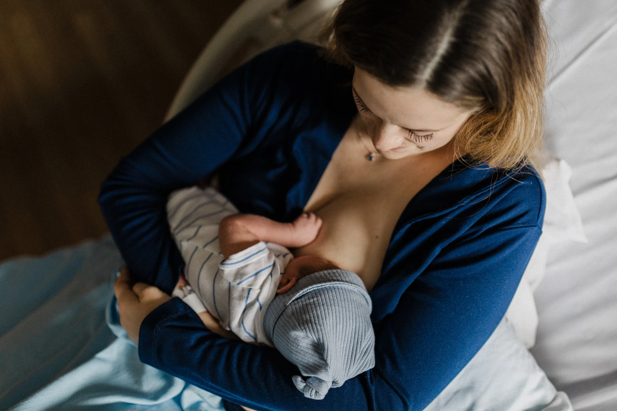 A woman breastfeeding a baby while sitting on a bed, seen from above.