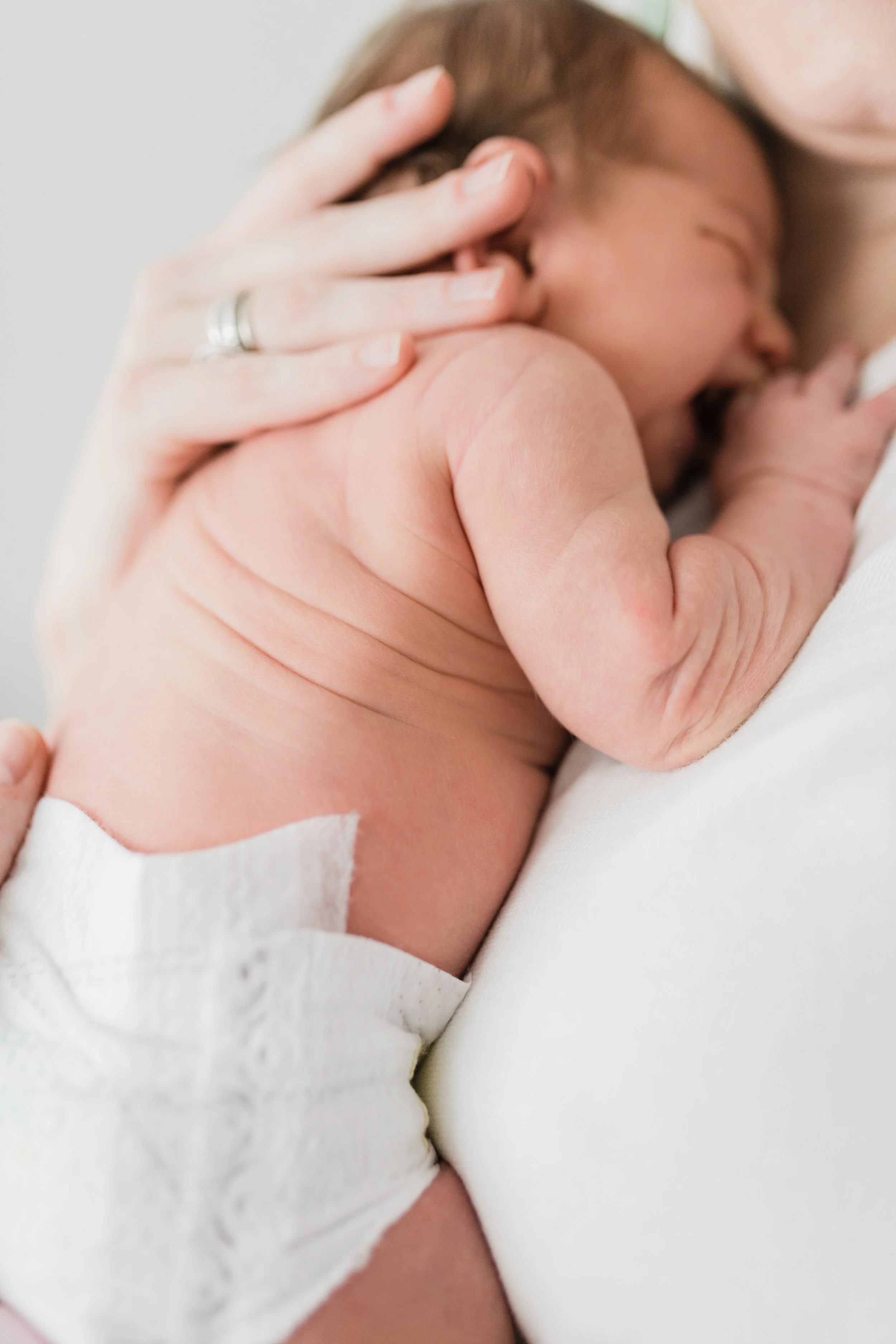 Close-up of a newborn baby held by an adult, the baby resting with eyes closed and mouth open, with part of an adult's hand supporting the baby's head and shoulder.