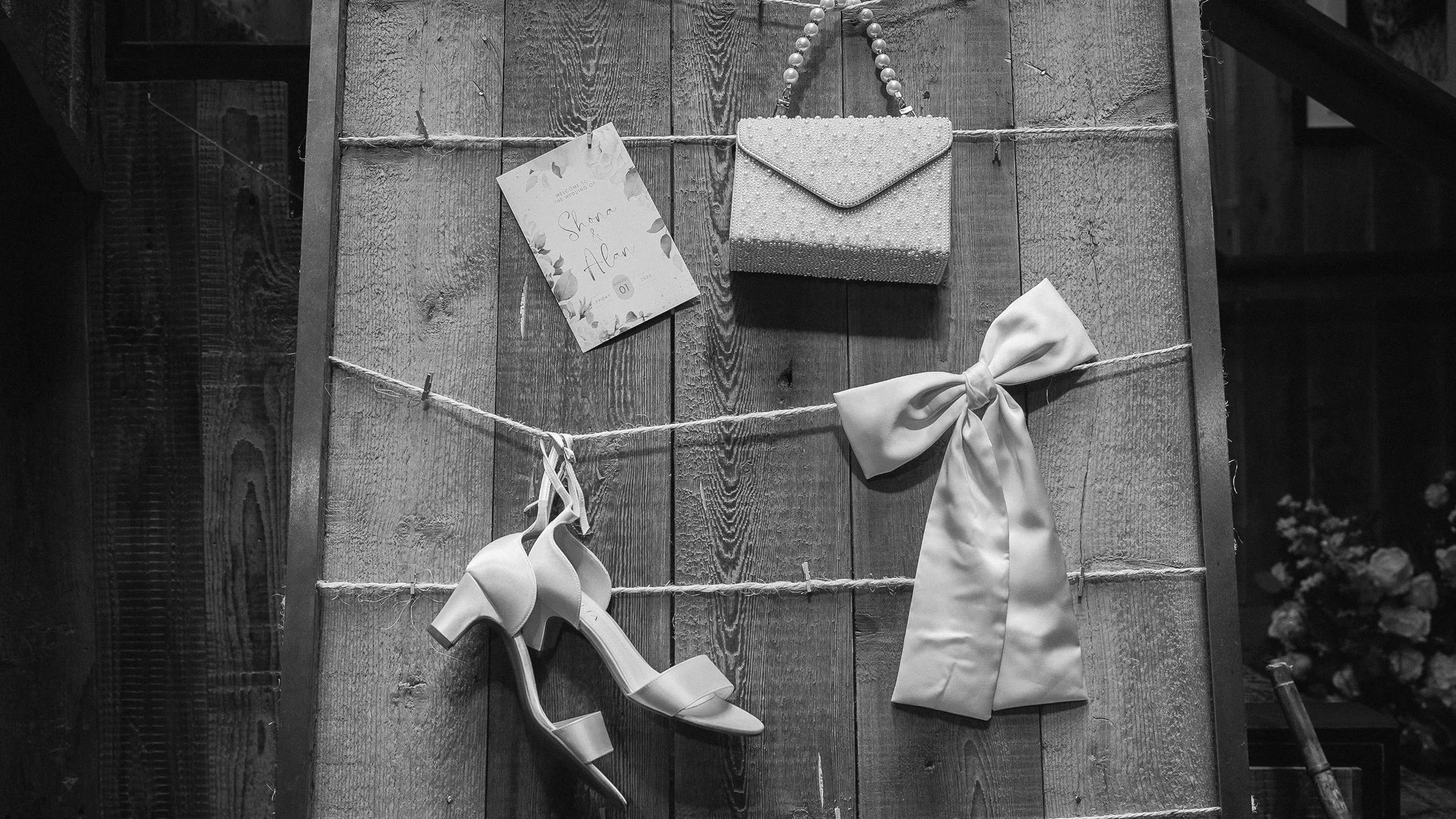 Wedding details on a wooden board: order of service, pearl bag, bridal sandals and satin bow – Glasson Lakehouse wedding