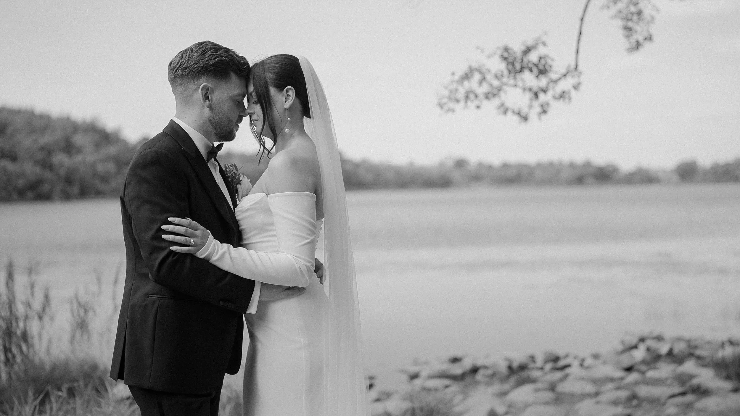 Black and white photo of the newlyweds embracing by the lake at Farnham Estate, Cavan