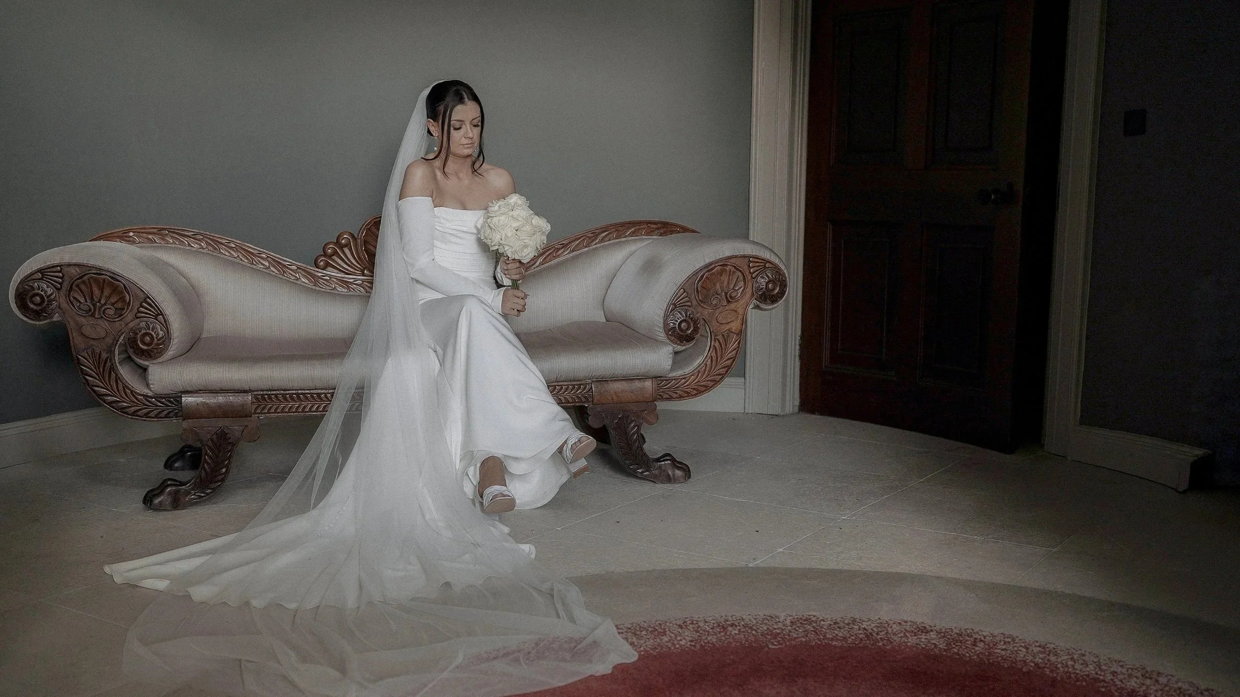 Bride sitting on an antique chaise inside the historic house at Farnham Estate