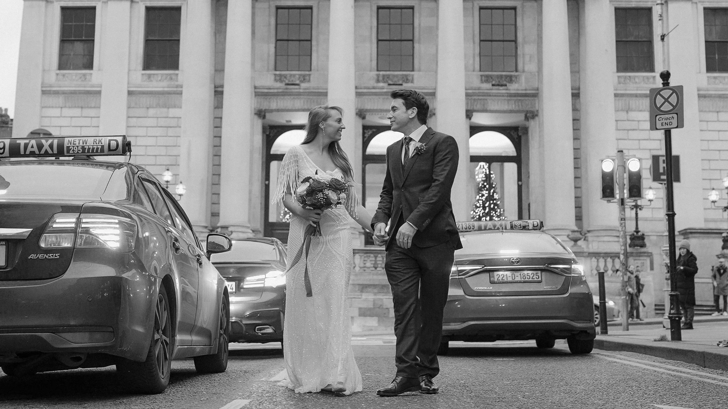 Bride and groom crossing Dame Street between taxis outside Dublin City Hall, black and white