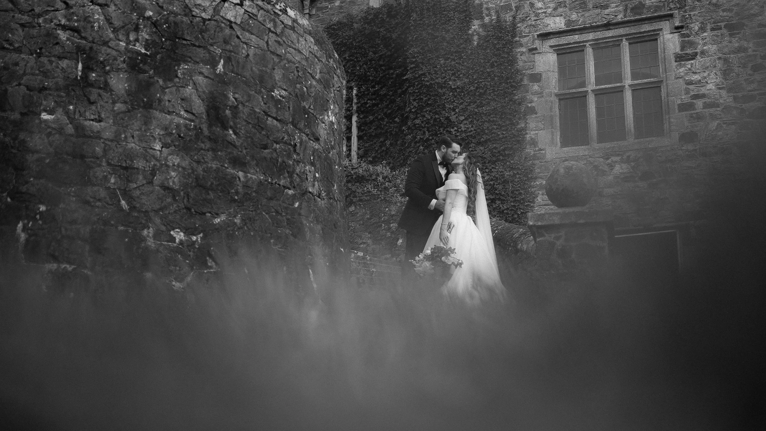 Bride and groom kissing by the ivy-covered tower of Waterford Castle, black and white