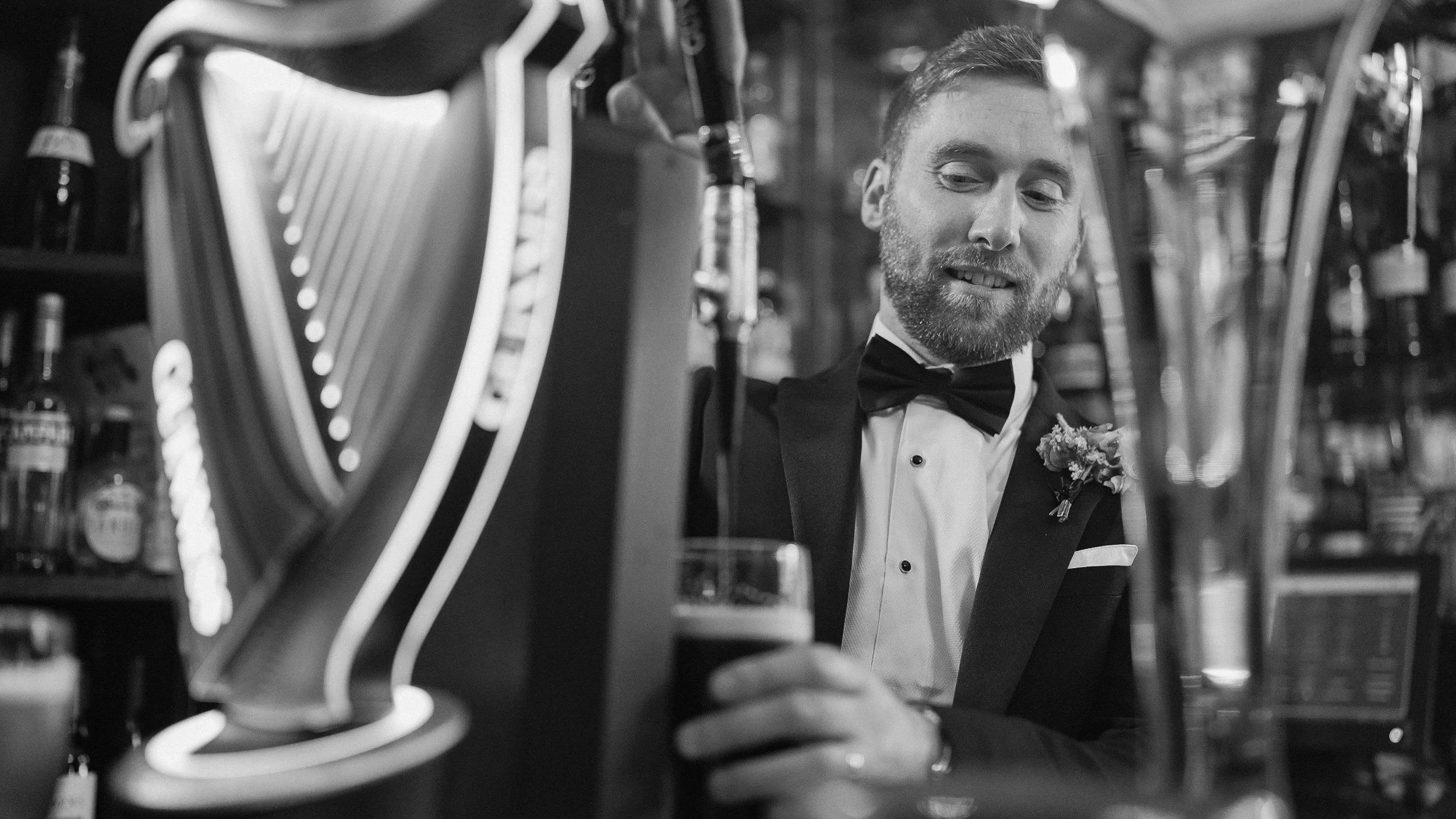 Groom pouring a pint of Guinness at the bar during his wedding at Tinakilly Country House, black and white