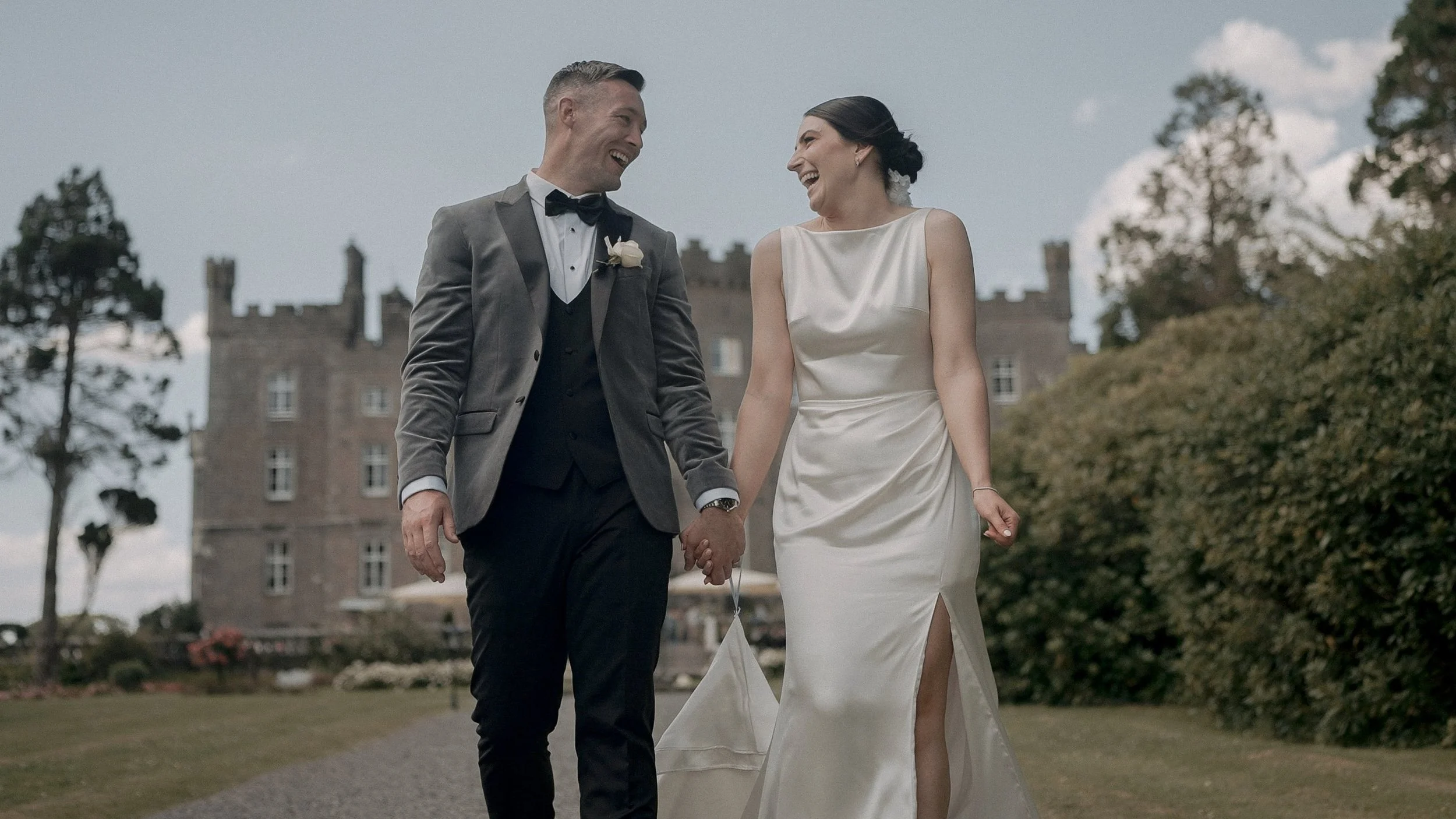 Laughing bride and groom walking hand in hand in front of Markree Castle, Co. Sligo