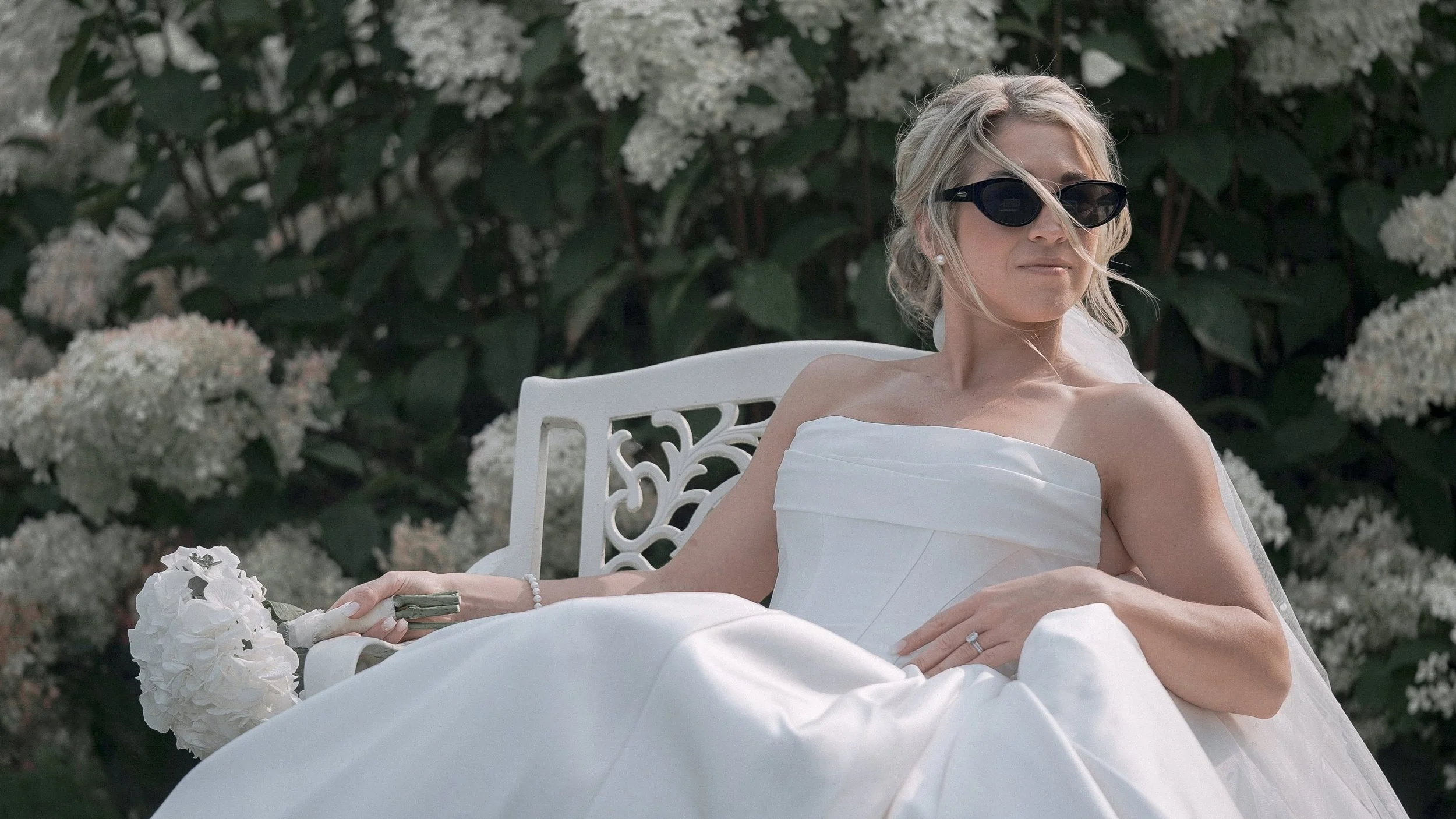 Bride in sunglasses on a white garden bench among hydrangeas, Kildare wedding