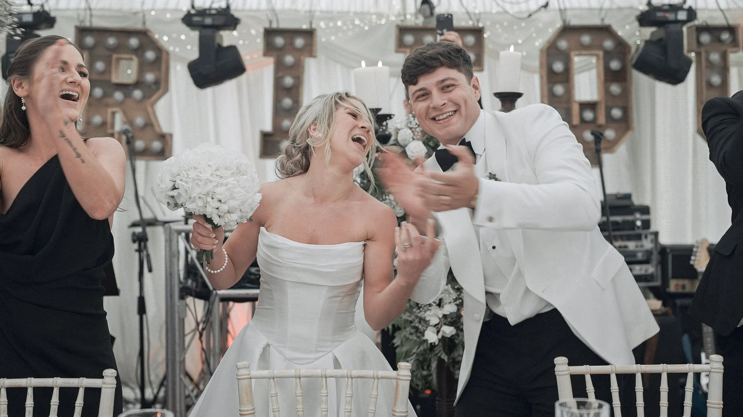 Bride and groom cheering at the top table in front of light-up letters, marquee wedding in Kildare