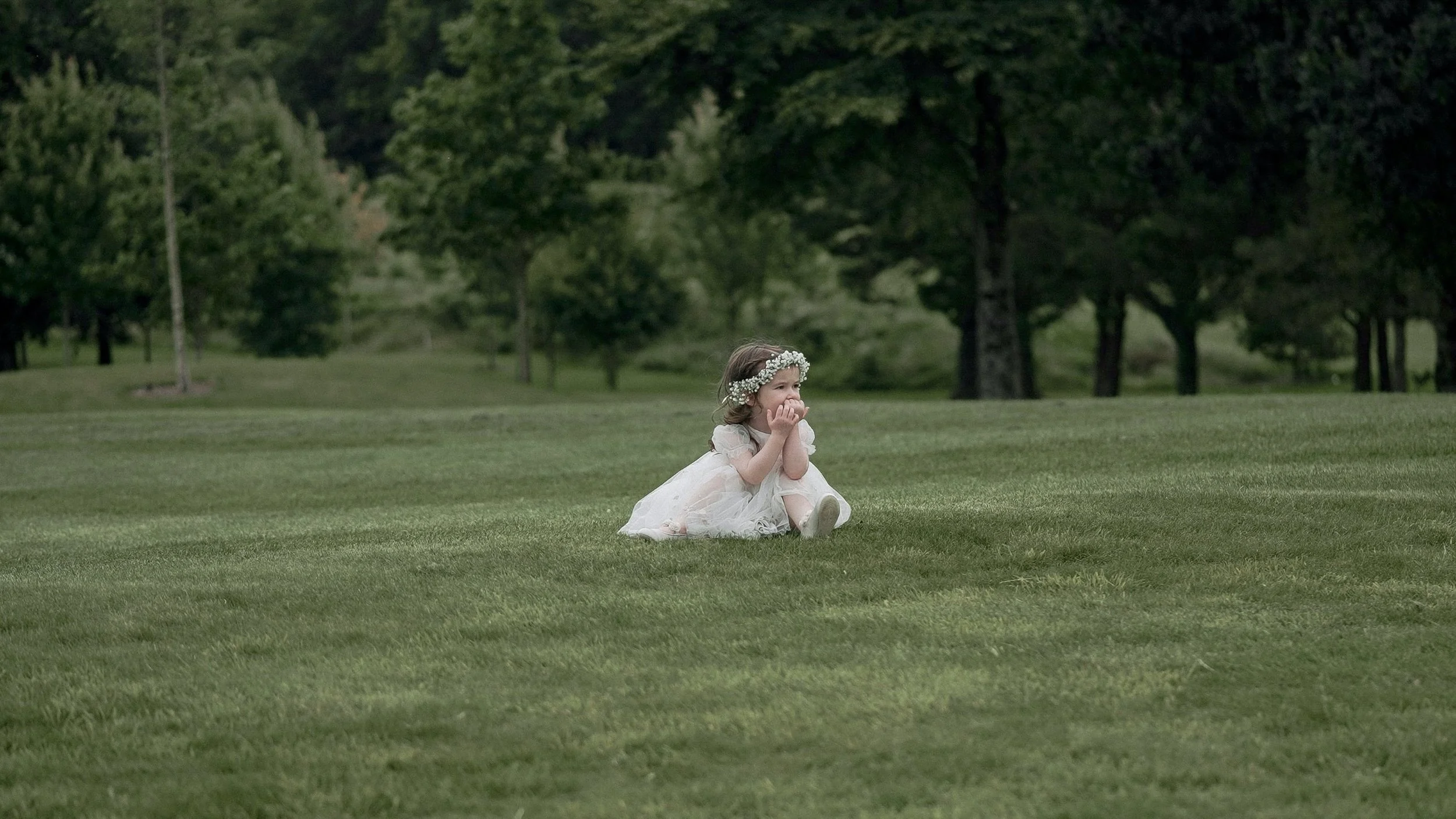 Flower girl with a gypsophila crown sitting on the lawn at Glasson Lakehouse wedding