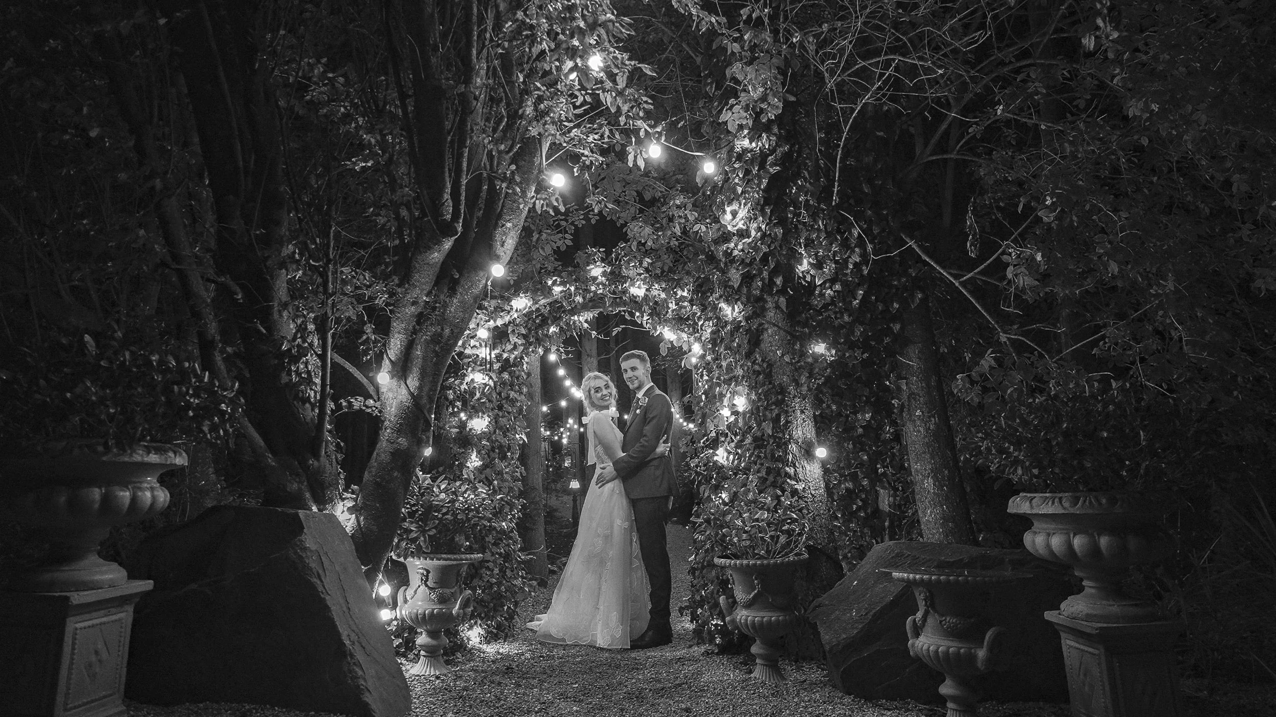 Black and white night portrait of the couple under an arch of festoon lights at the Station House Hotel
