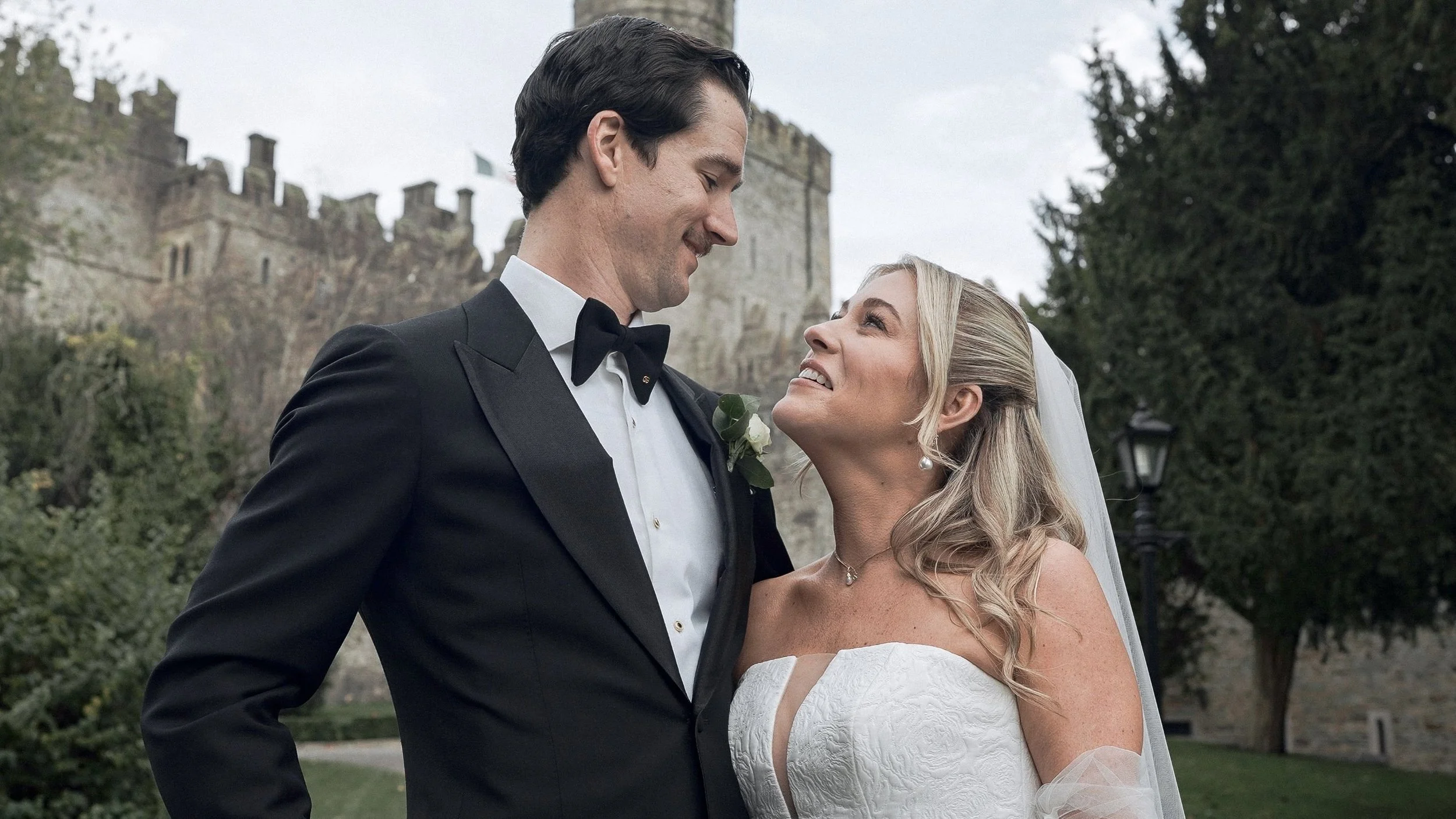 Bride and groom smiling at each other beneath the tower of Kilkea Castle, Co. Kildare