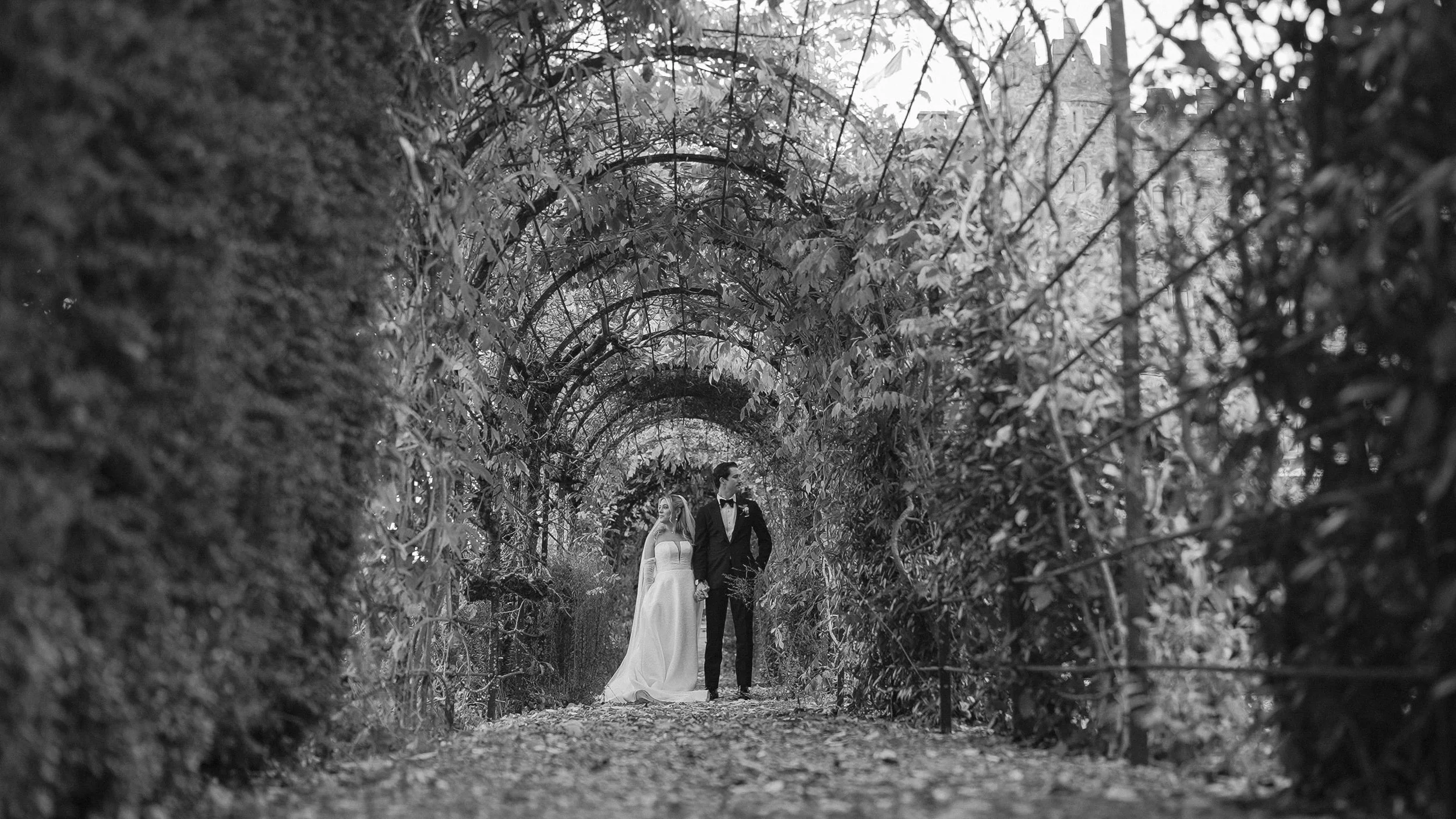 Black and white photo of the couple under the garden arches at Kilkea Castle, Castledermot