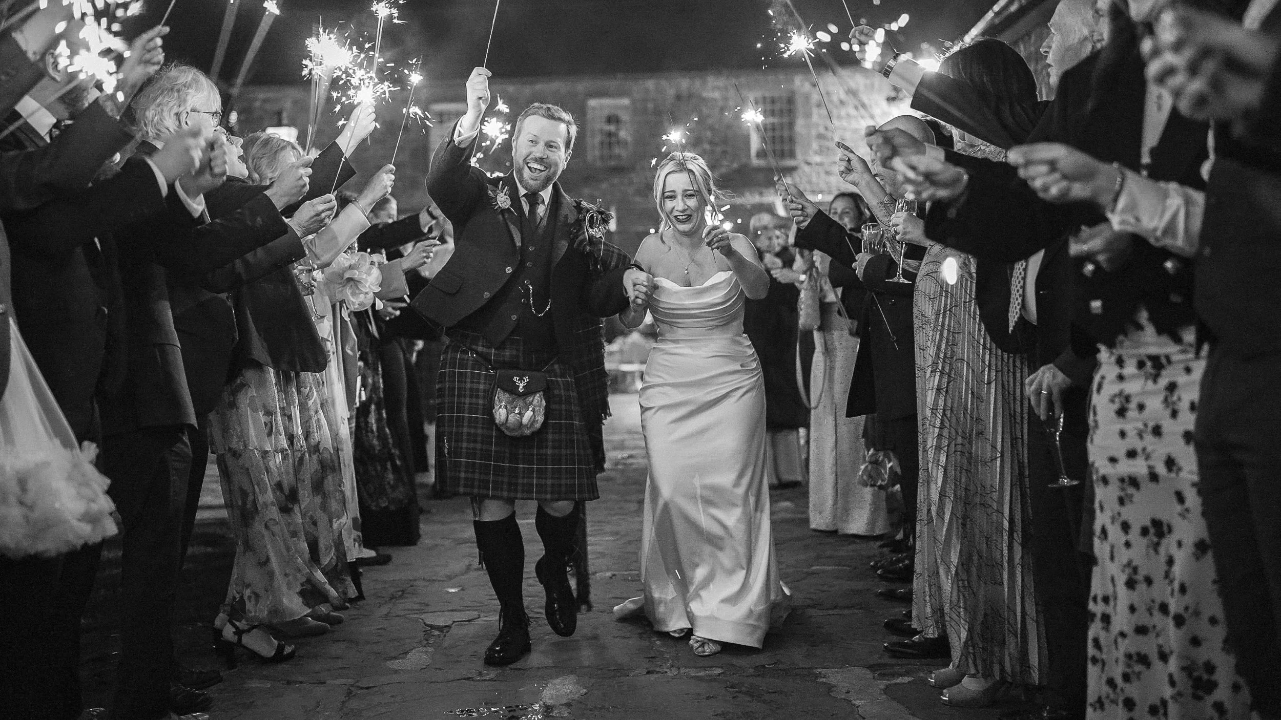 Bride and groom in a kilt running through a sparkler tunnel at Ballymagarvey Village, Co. Meath