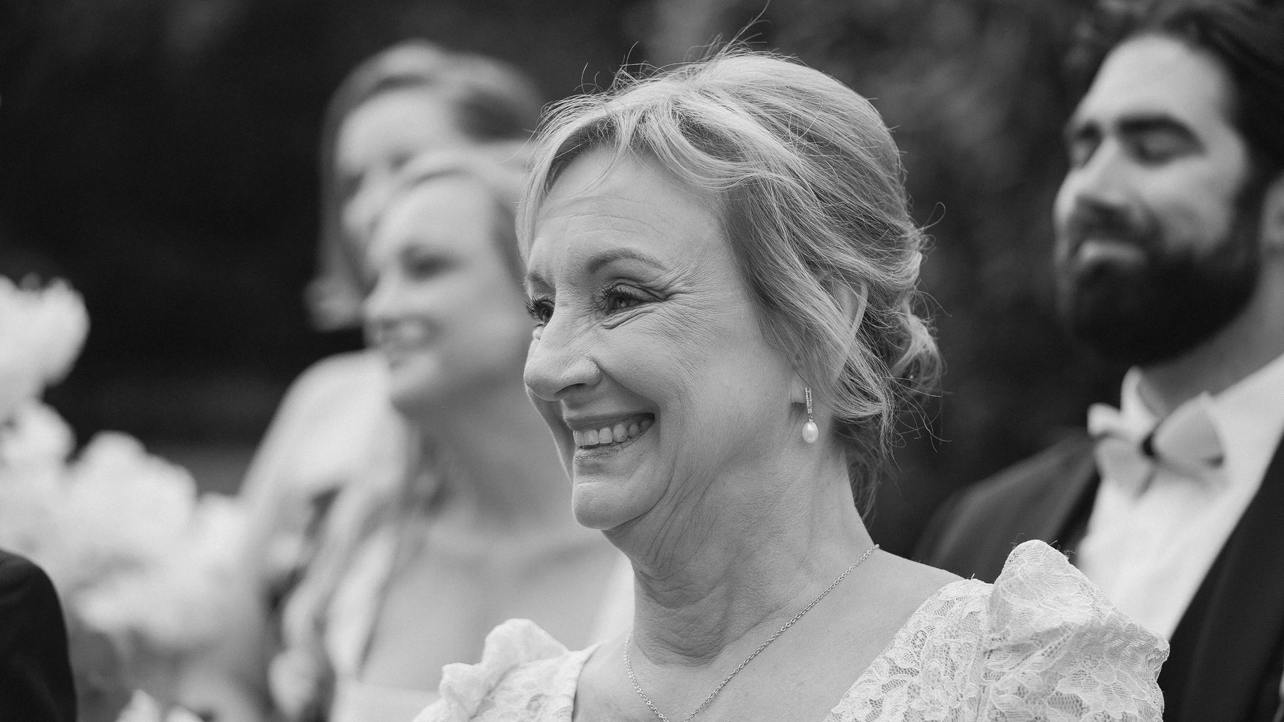 Mother of the bride smiling during the outdoor wedding ceremony at Waterford Castle, black and white