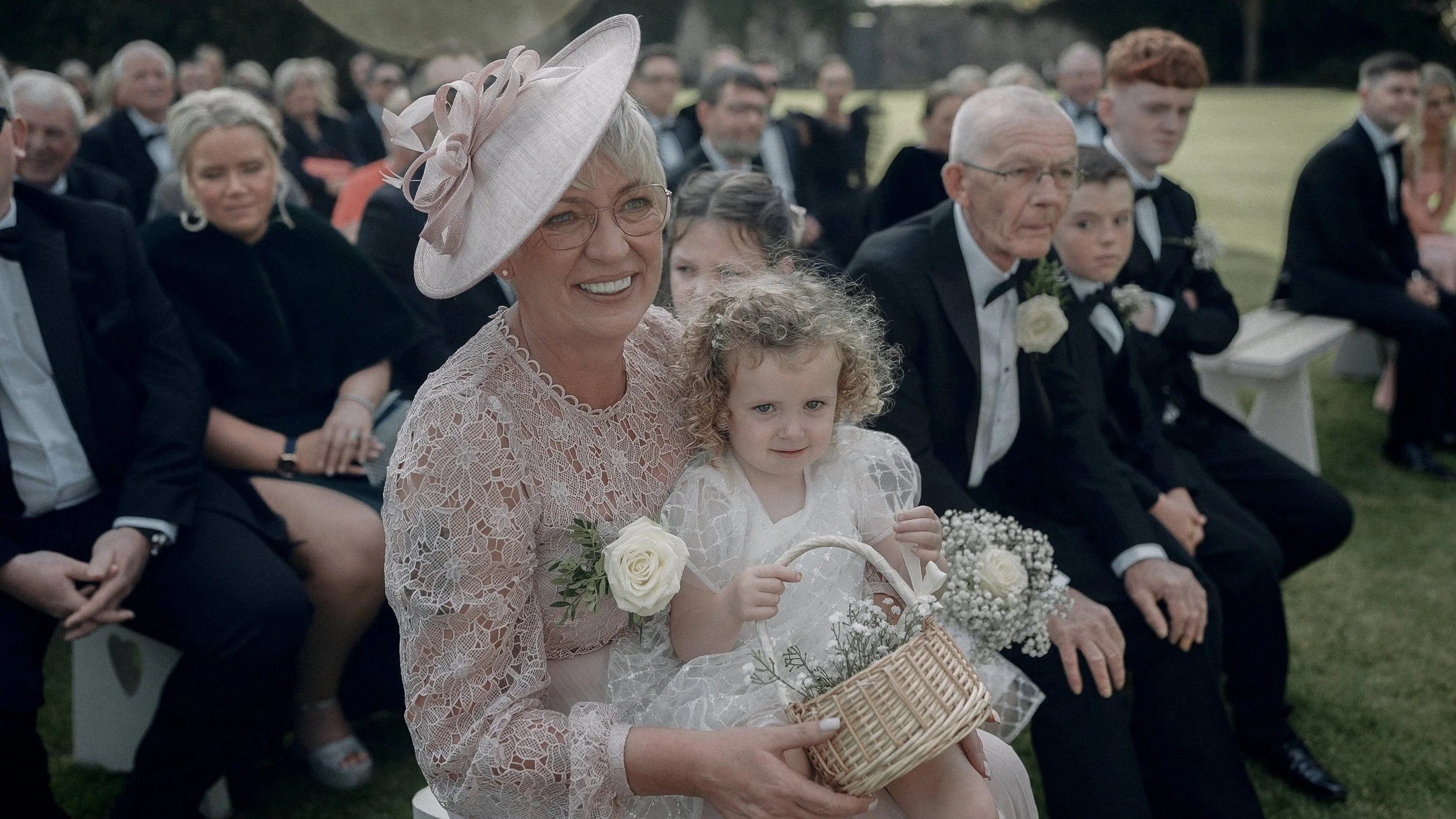 Flower girl with a basket of gypsophila sitting with guests at the Farnham Estate wedding ceremony
