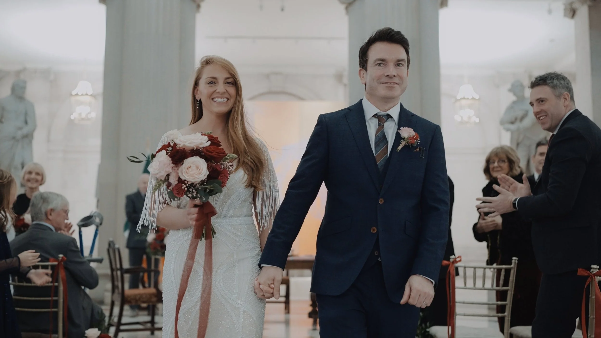 Bride and groom walking back down the aisle in the Rotunda of Dublin City Hall as guests applaud
