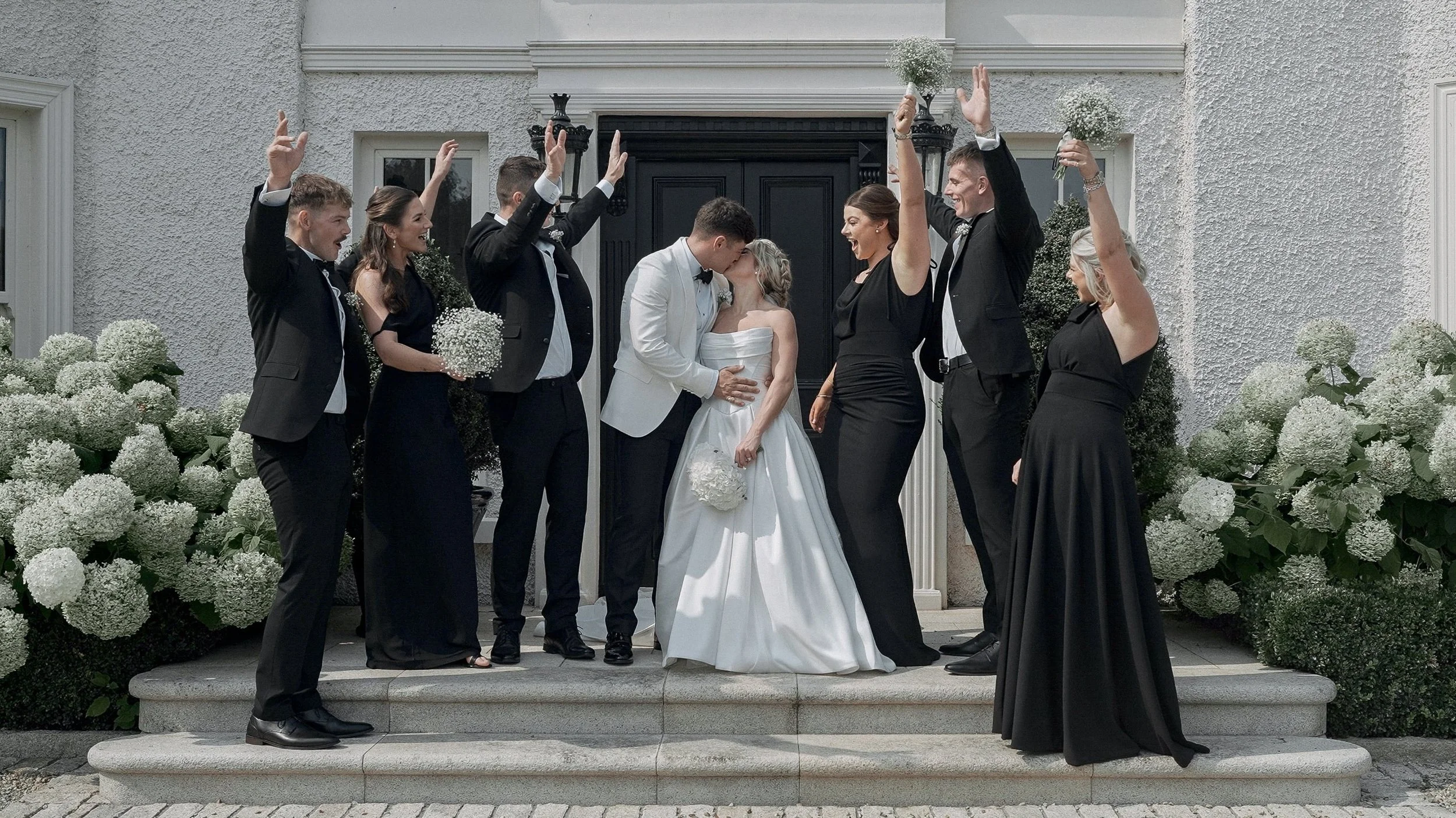 Bridal party cheering as Taylor and Jack kiss at the front door of their family home on The Curragh