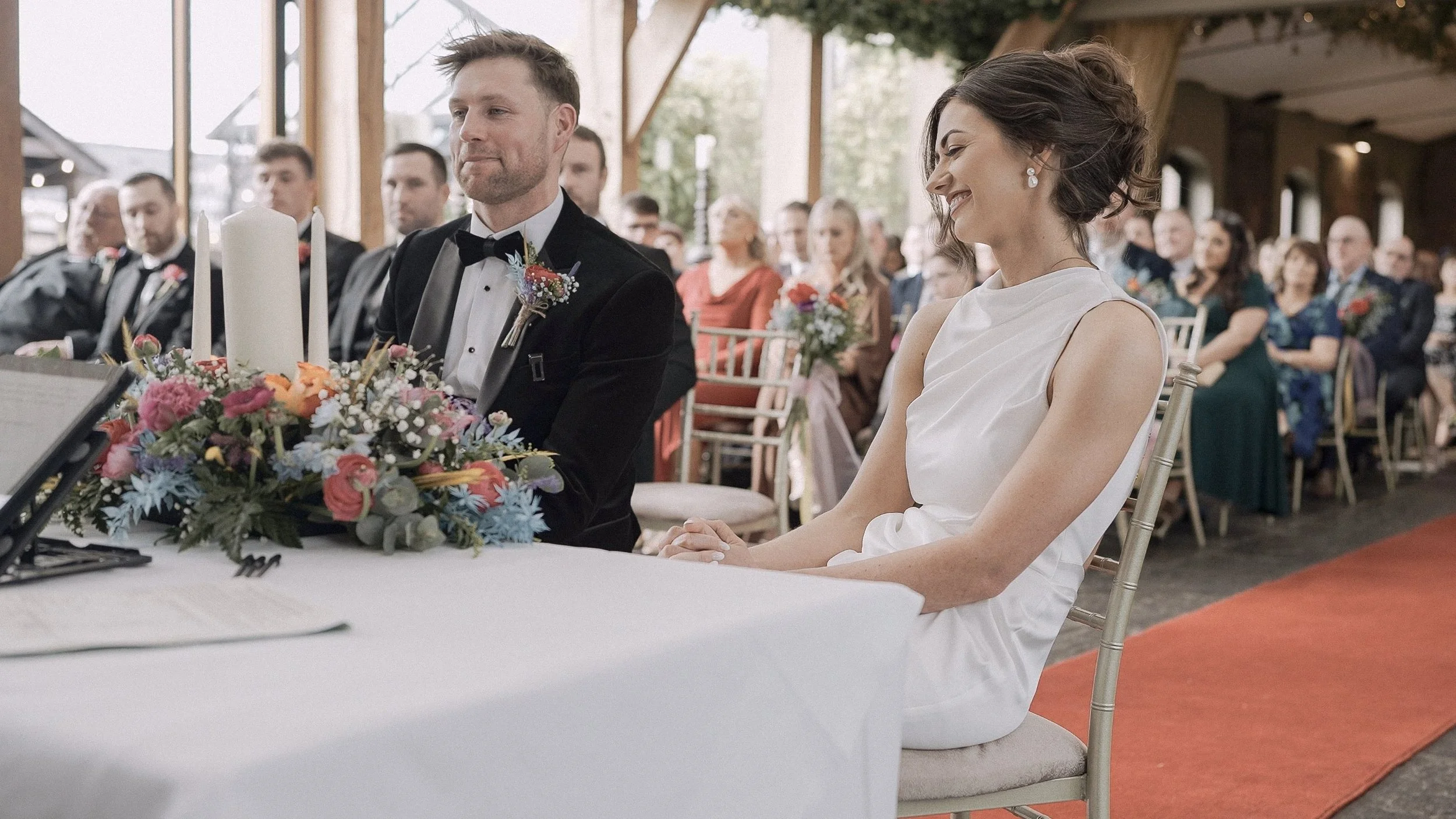 Bride and groom smiling at the ceremony table with colourful flowers and candles at Barberstown Castle