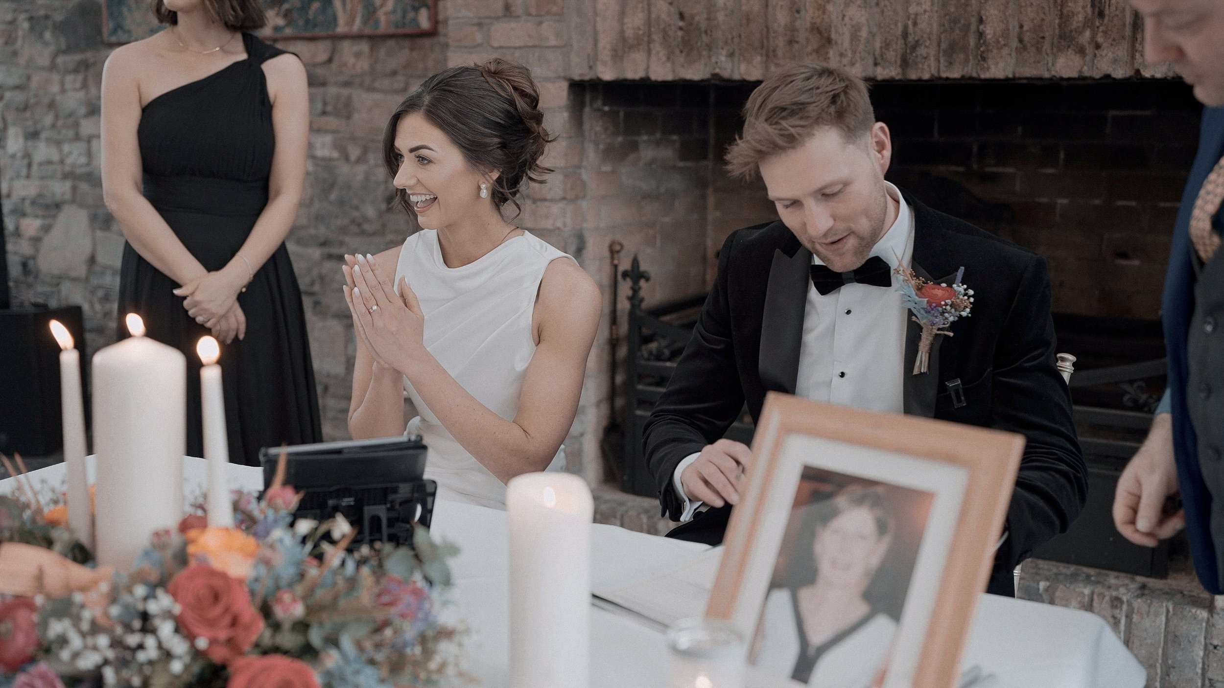 Bride and groom signing the register by the fireplace with a framed photo of a loved one at Barberstown Castle