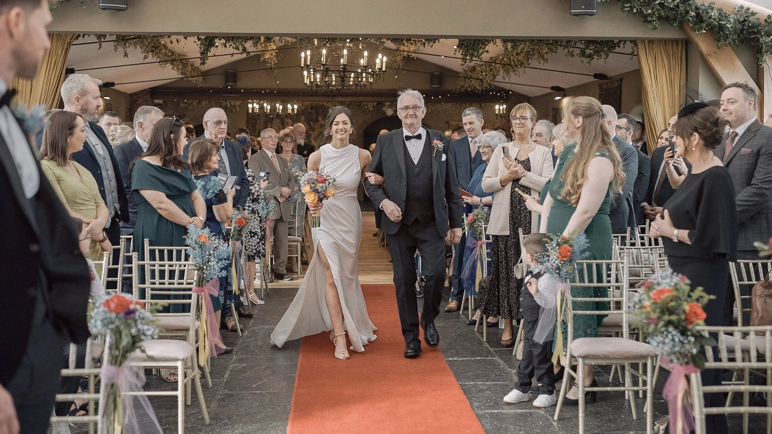 Bride walking down the red carpet aisle with her father in the Banquet Hall at Barberstown Castle