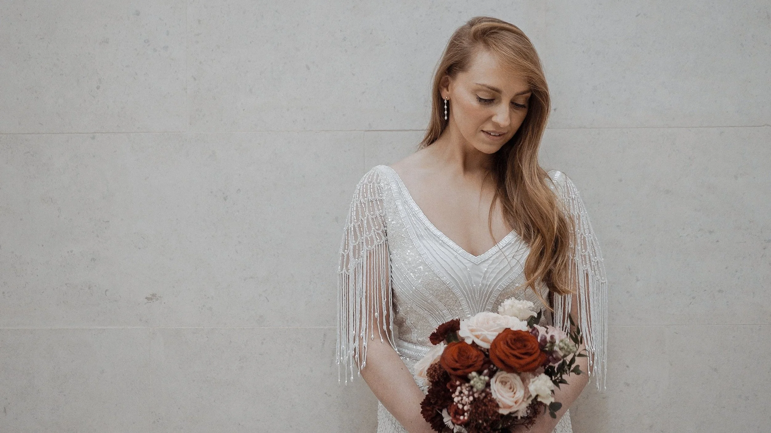 Bride looking down at her bouquet against the stone wall of Dublin City Hall
