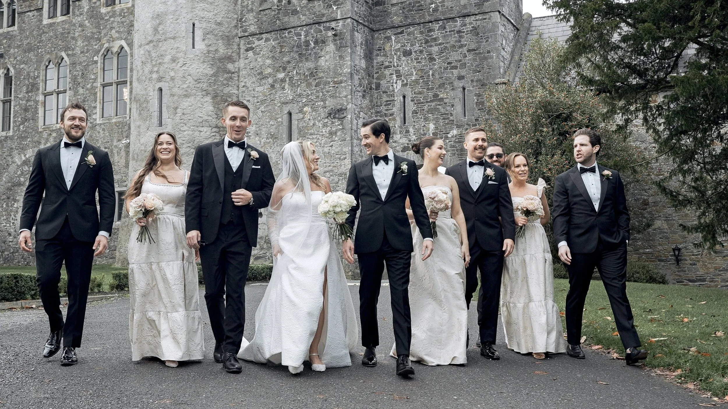 Bride, groom and bridal party in black tie walking in front of Kilkea Castle, Co. Kildare
