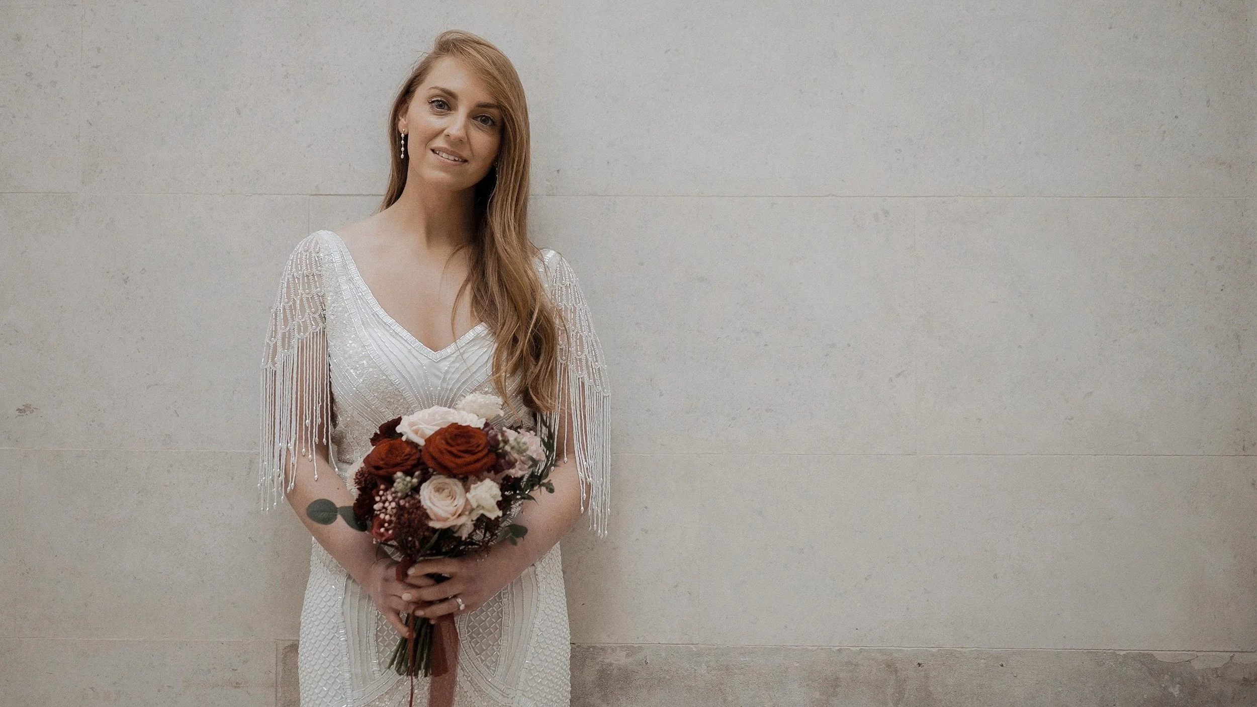 Bride in a beaded fringe-sleeve gown with a red and blush rose bouquet at Dublin City Hall