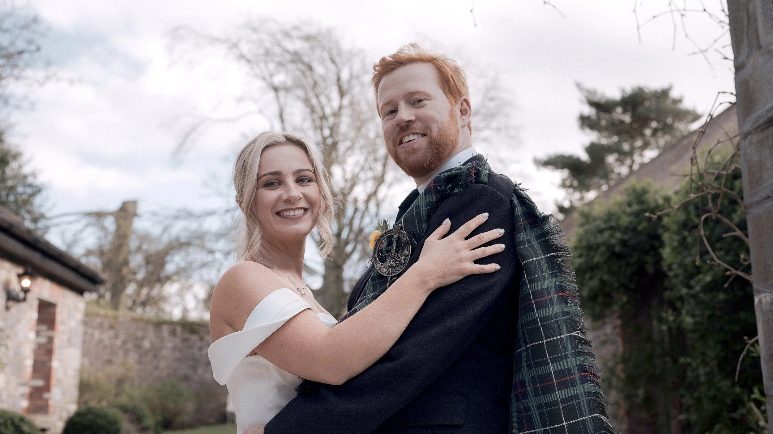 Bride and groom in a tartan kilt smiling in the courtyard at Ballymagarvey Village, Co. Meath
