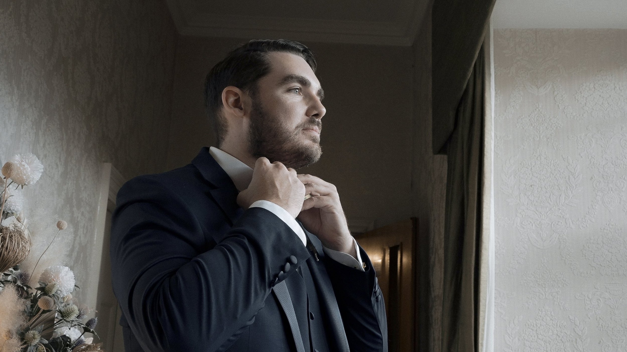 Groom adjusting his bow tie by the window while getting ready at Waterford Castle