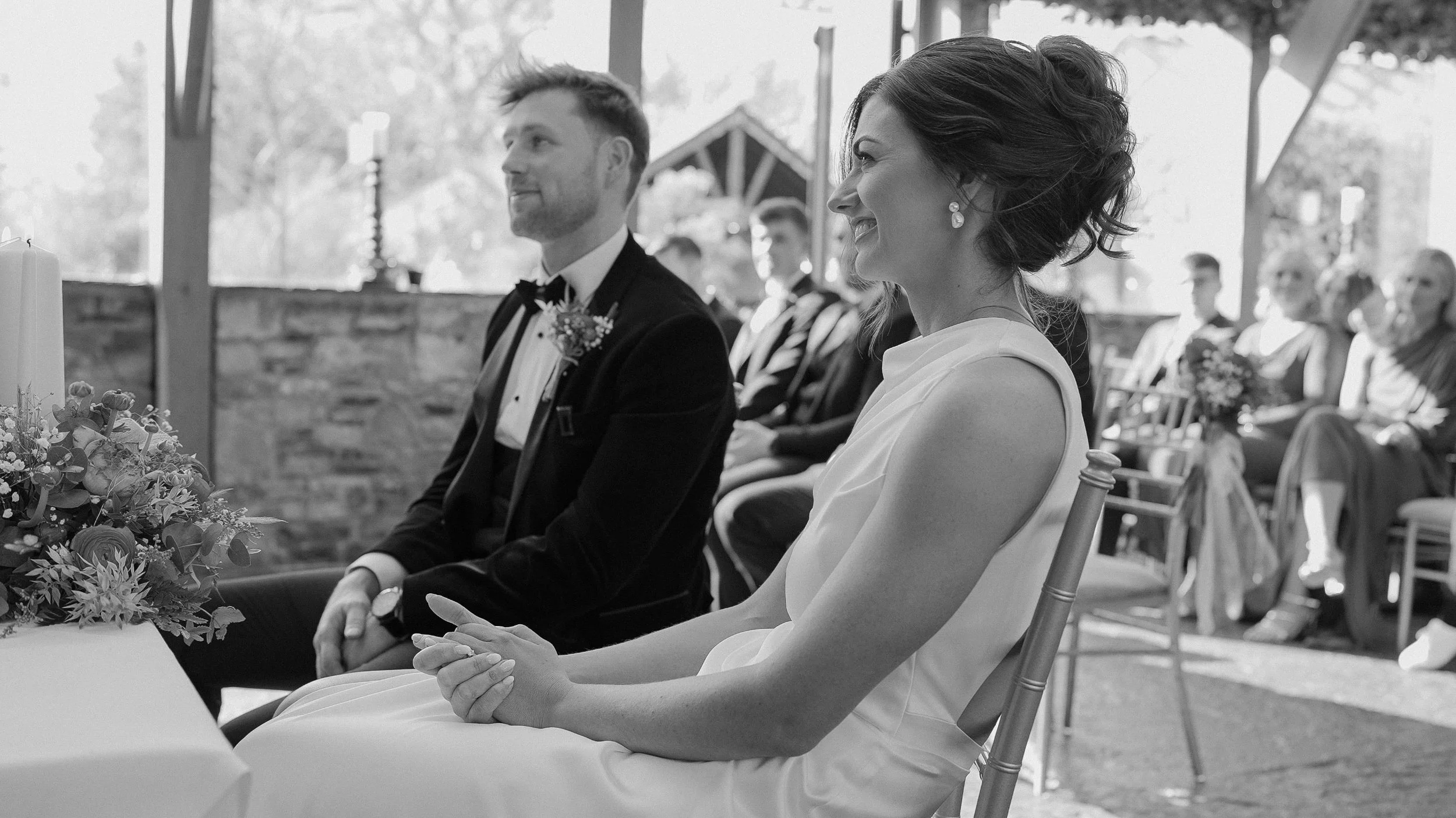 Smiling bride and groom seated during their wedding ceremony at Barberstown Castle, black and white