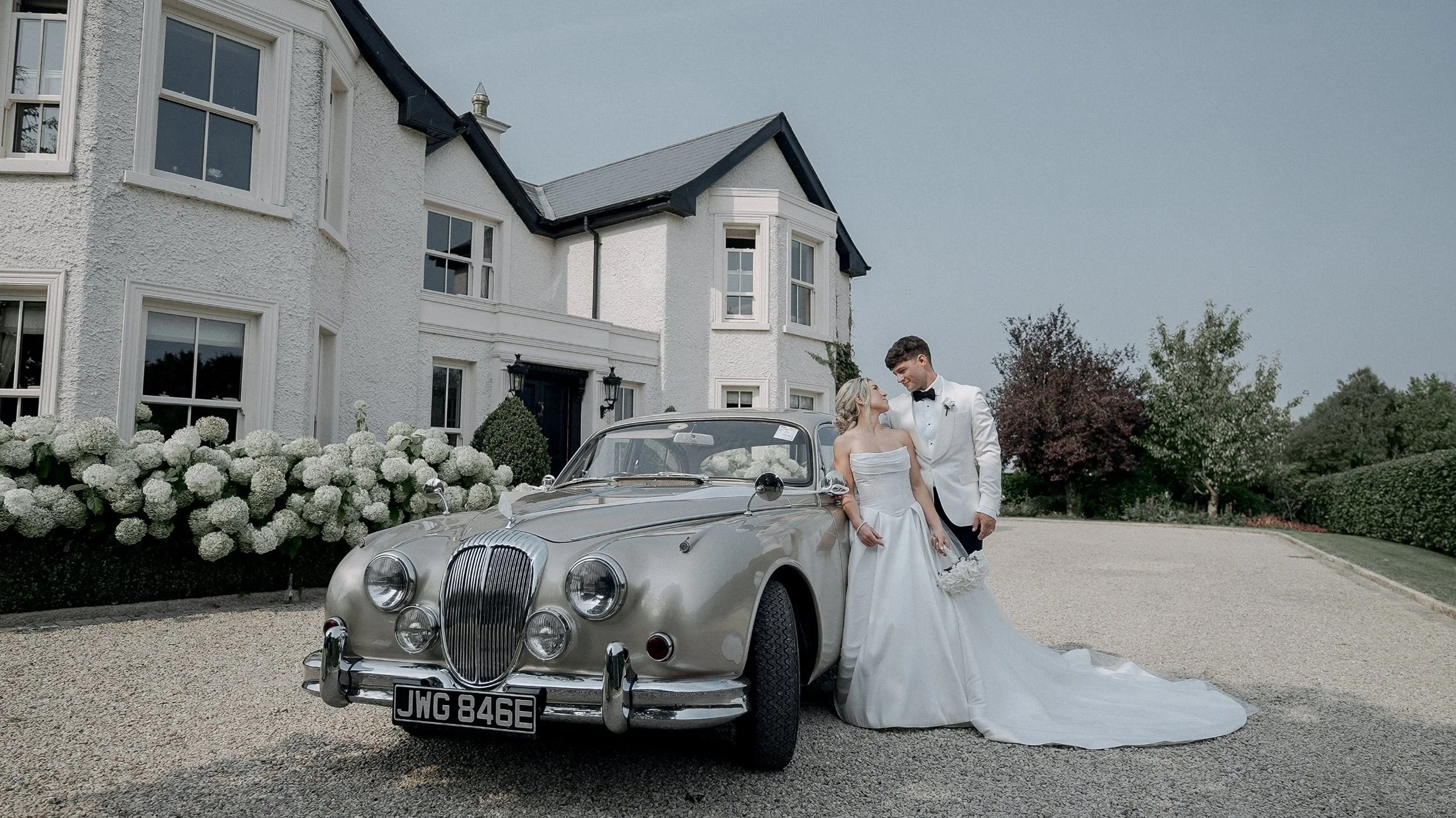 Taylor and Jack with a classic vintage wedding car outside their family home on The Curragh, Kildare
