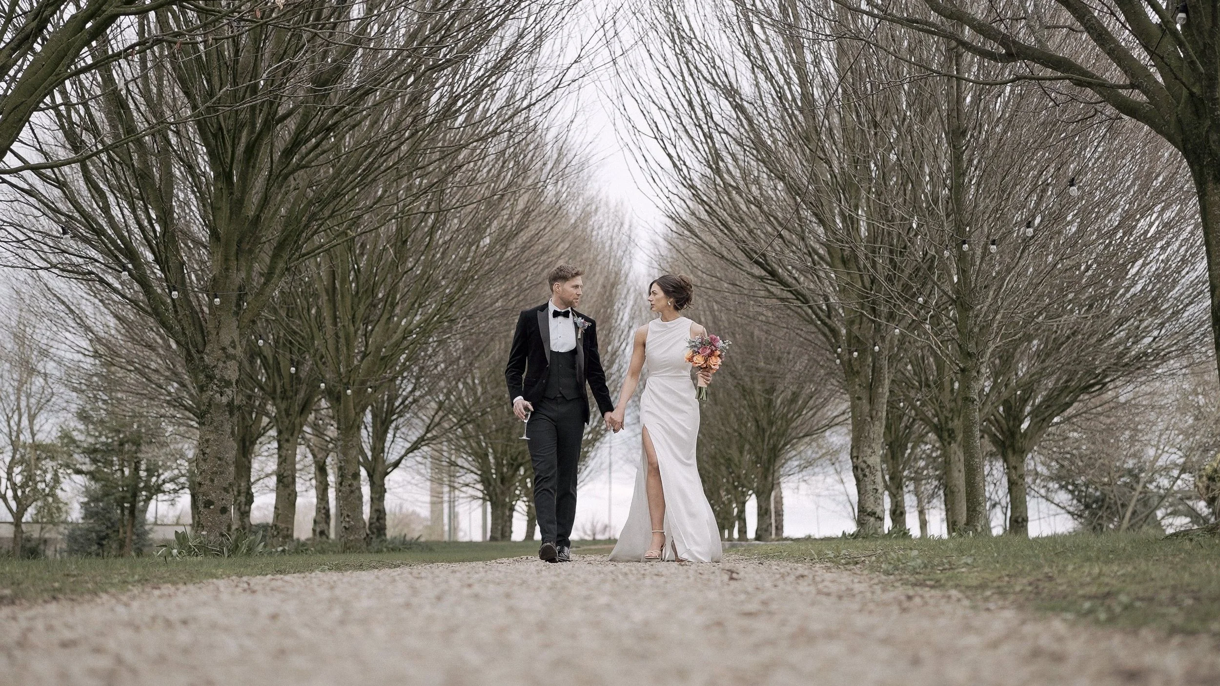 Bride and groom walking hand in hand along the tree-lined avenue at Barberstown Castle, Co. Kildare