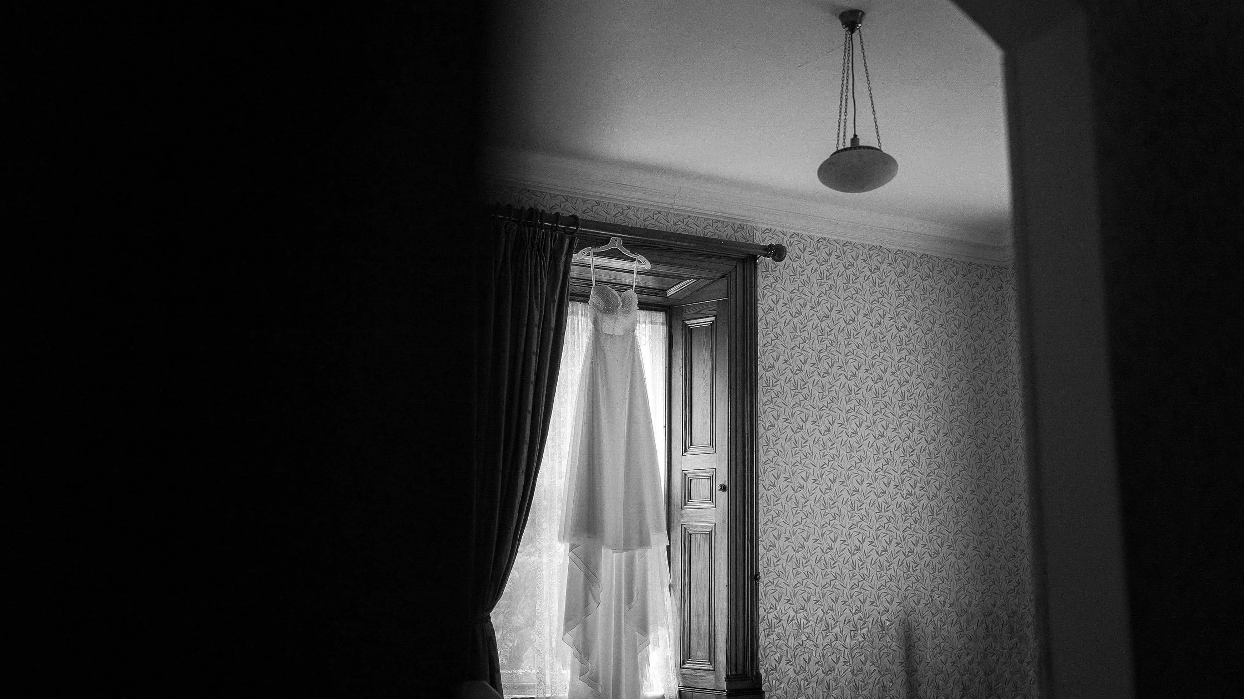 Black and white photo of the wedding dress hanging in a period window at Tinakilly House, Co. Wicklow