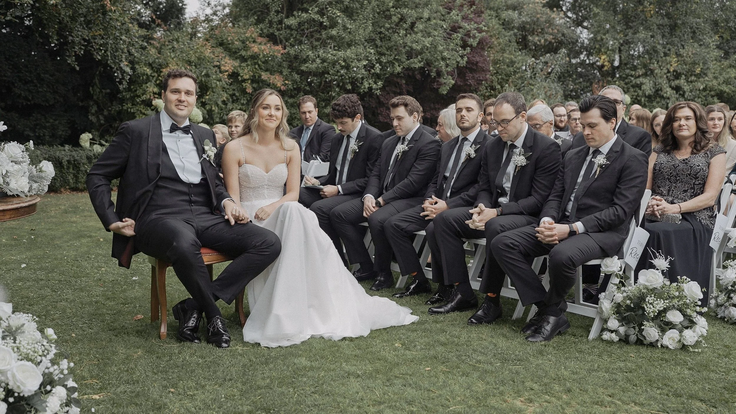 Catherine and Chris seated beside their groomsmen during the garden ceremony at Tinakilly House