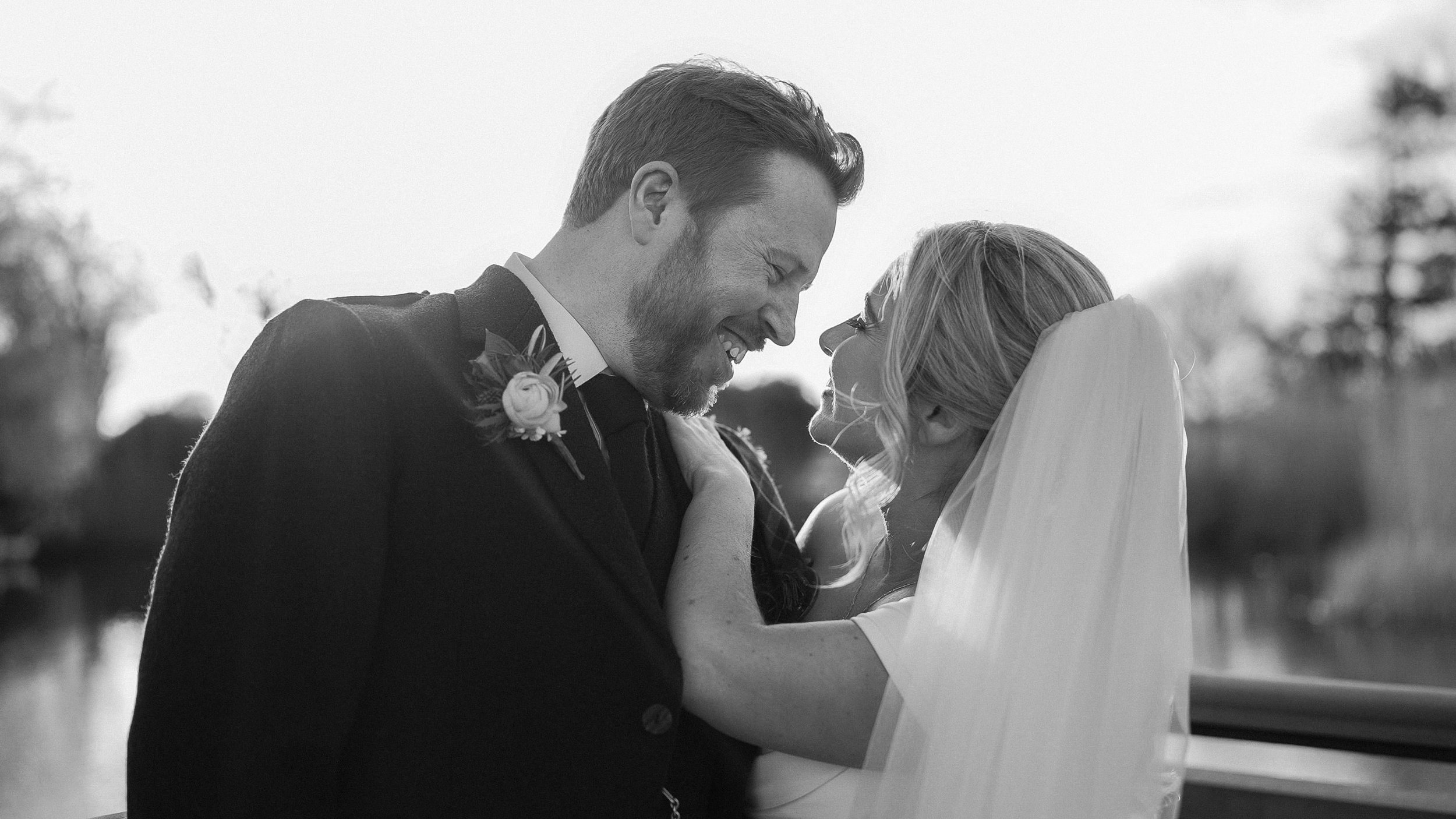 Black and white portrait of the laughing bride and groom by the lake at Ballymagarvey Village