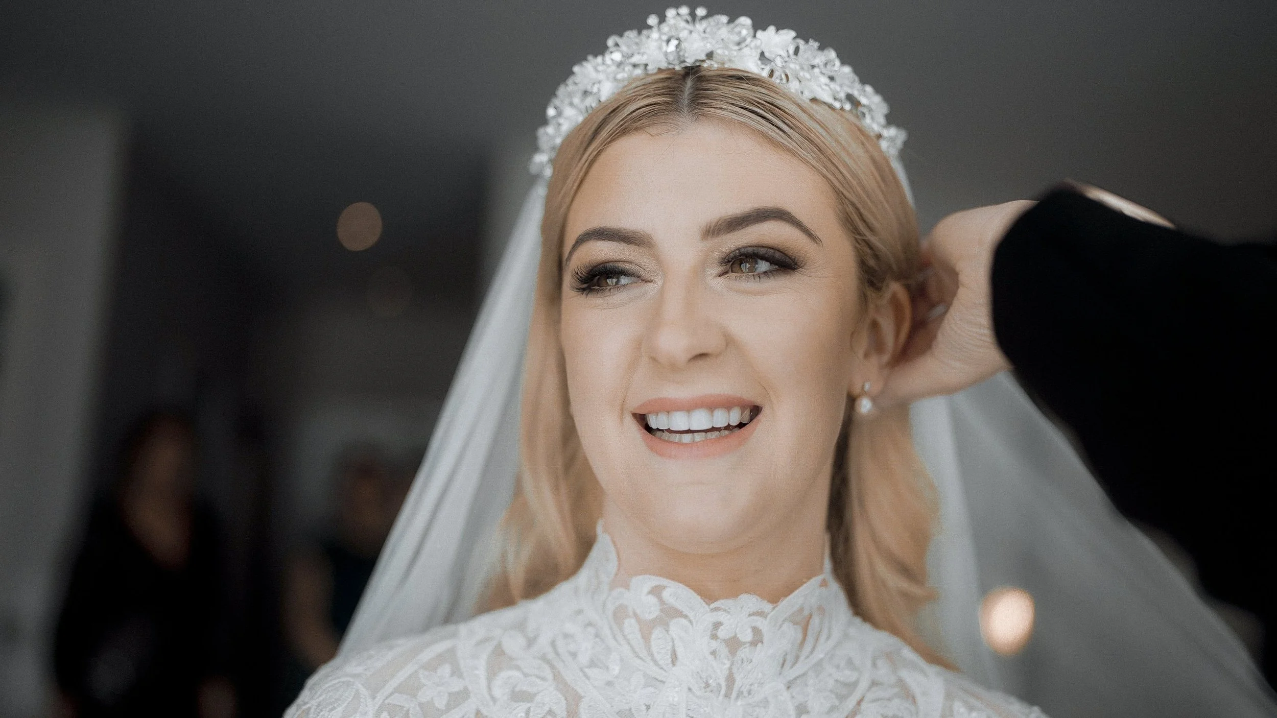 Smiling bride in a high-neck lace wedding dress, tiara and veil getting ready at the Armada Hotel, Spanish Point