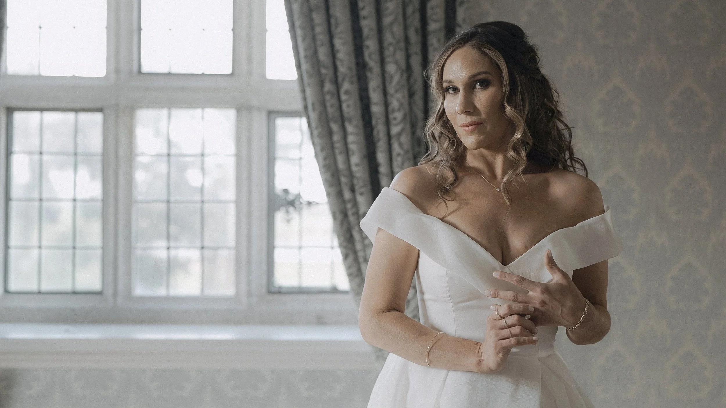 Bride in an off-the-shoulder wedding gown by a leaded window inside Waterford Castle