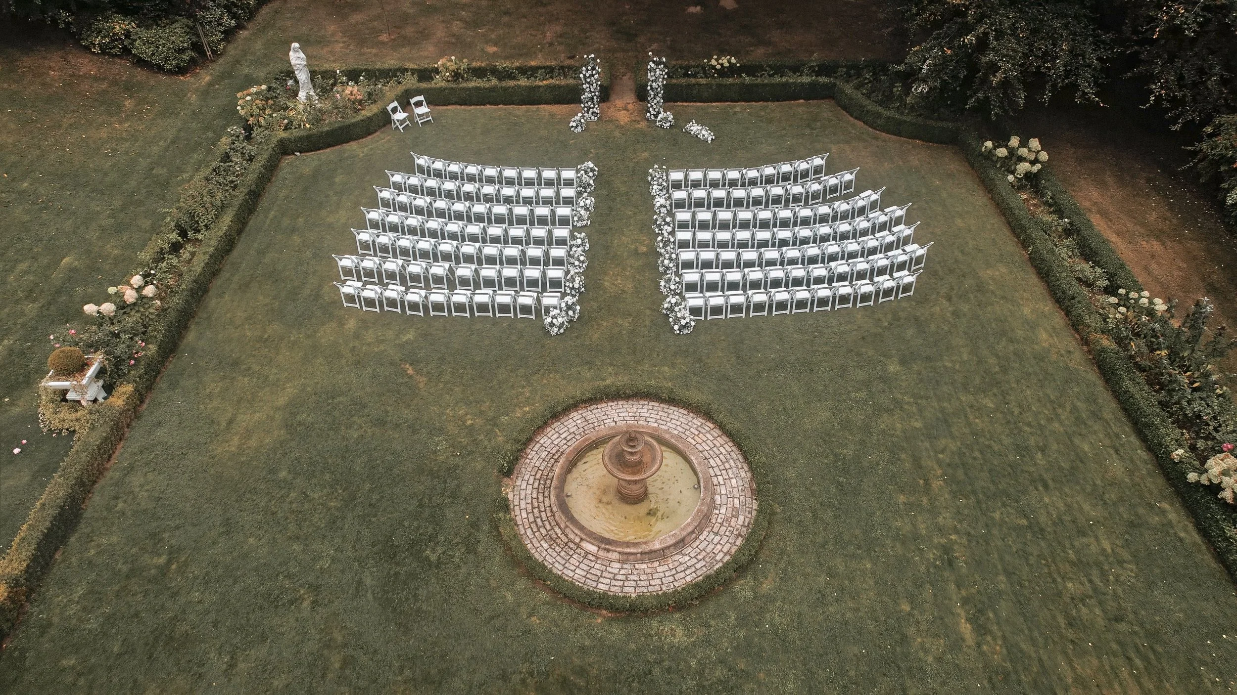 Aerial view of an outdoor wedding ceremony set-up with white chairs and a fountain in the garden at Tinakilly House