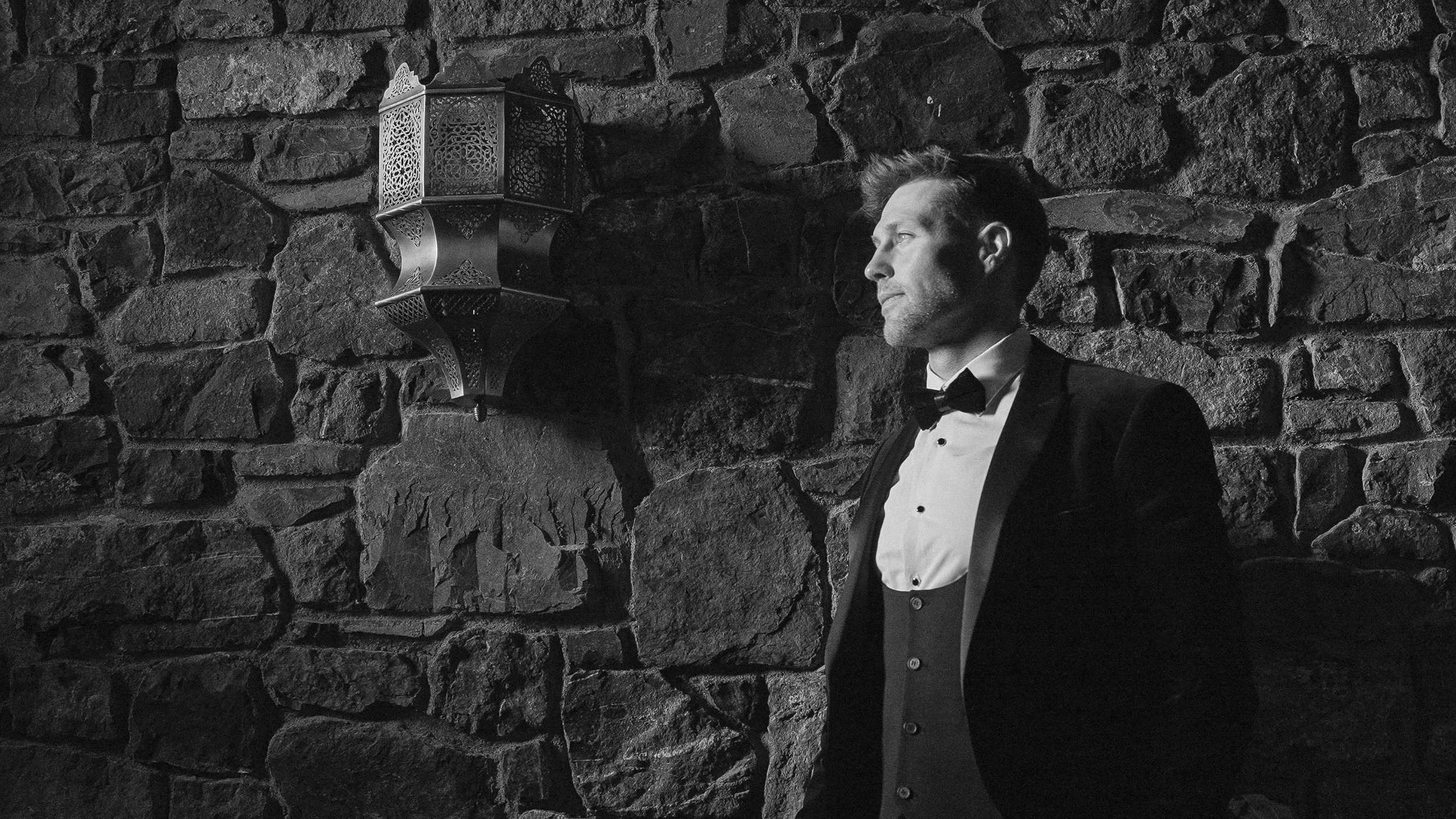 Groom in a tuxedo against the old stone wall of Barberstown Castle, black and white portrait