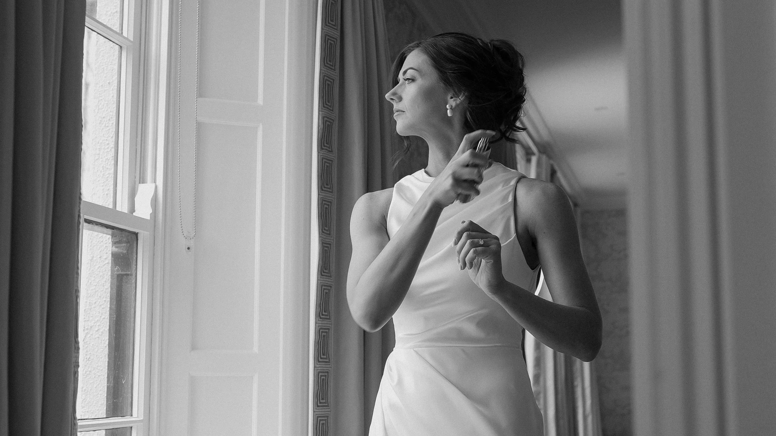 Bride putting on perfume by the window on her wedding morning at Barberstown Castle, black and white