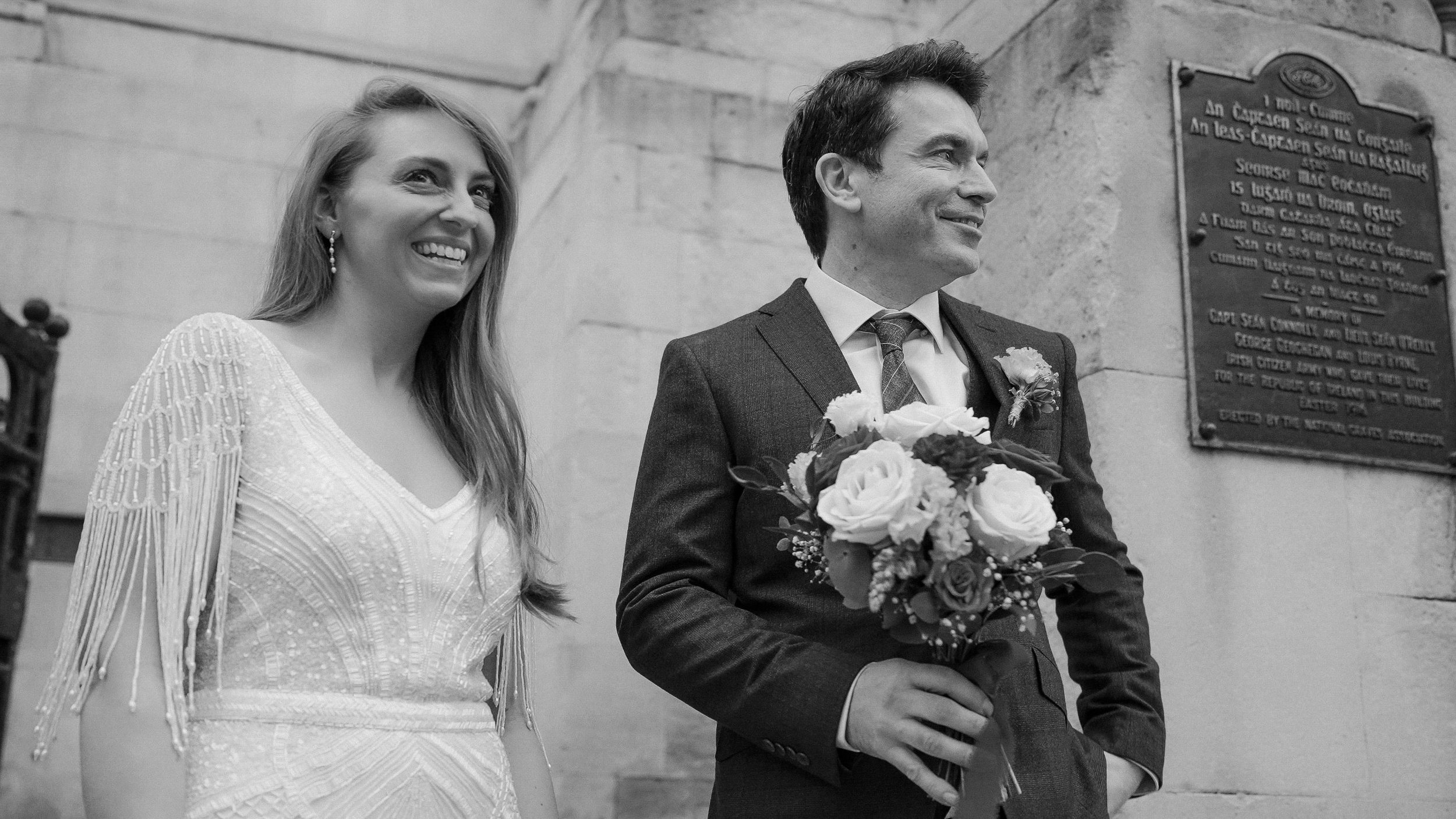 Bride and groom smiling beside the 1916 memorial plaque outside Dublin City Hall, black and white