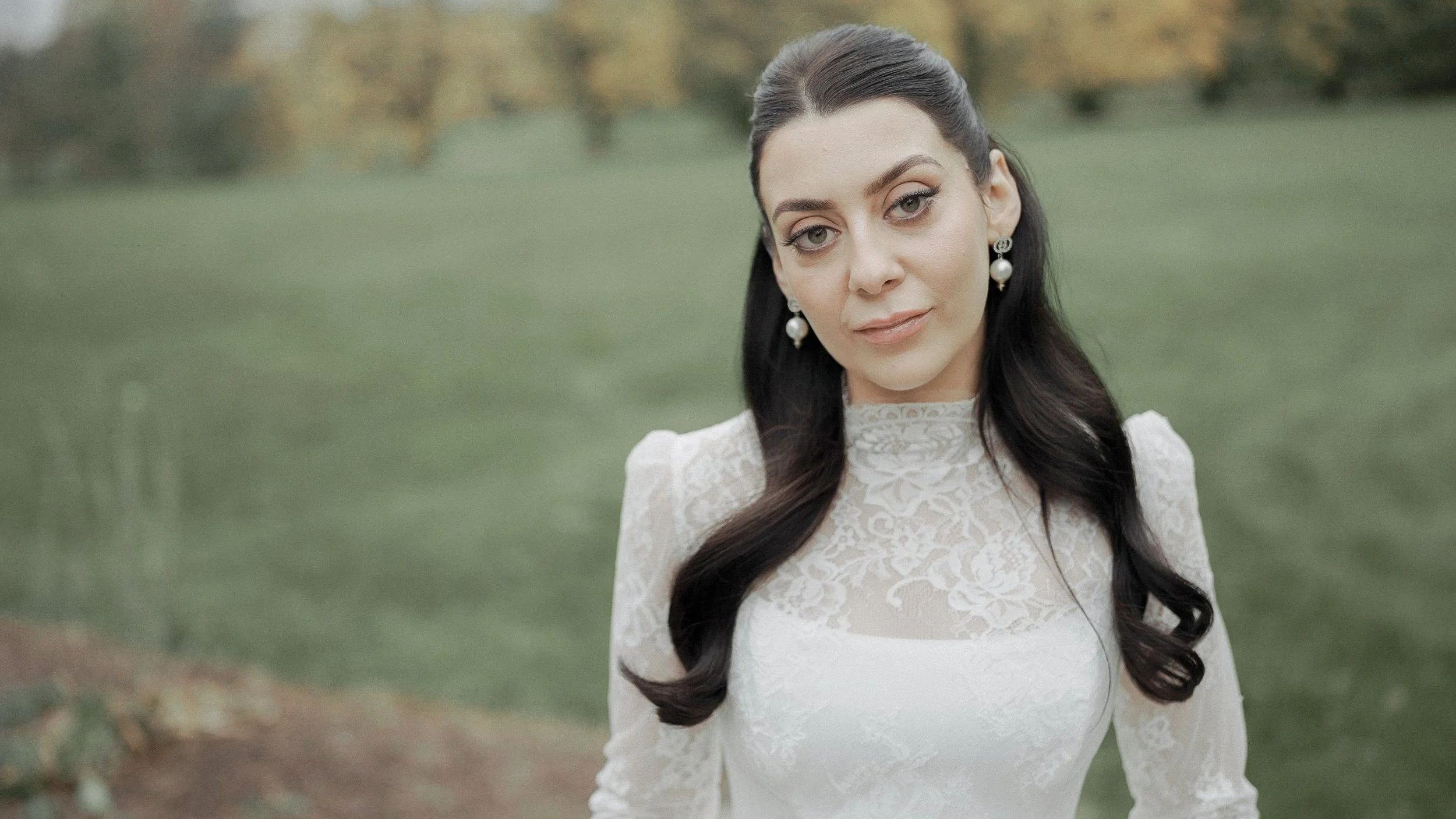 Bride portrait in a high-neck lace wedding gown and pearl earrings on the grounds of Kilkea Castle