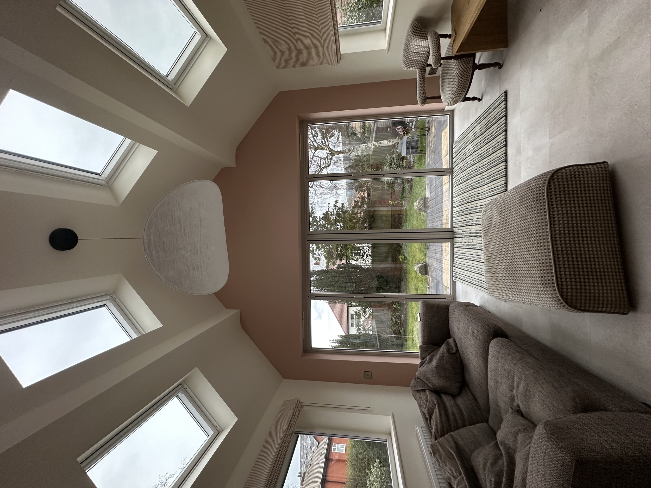Living room with large windows, a sofa, two patterned chairs, a striped rug, a glass sliding door leading to a garden, and a hanging pendant light.
